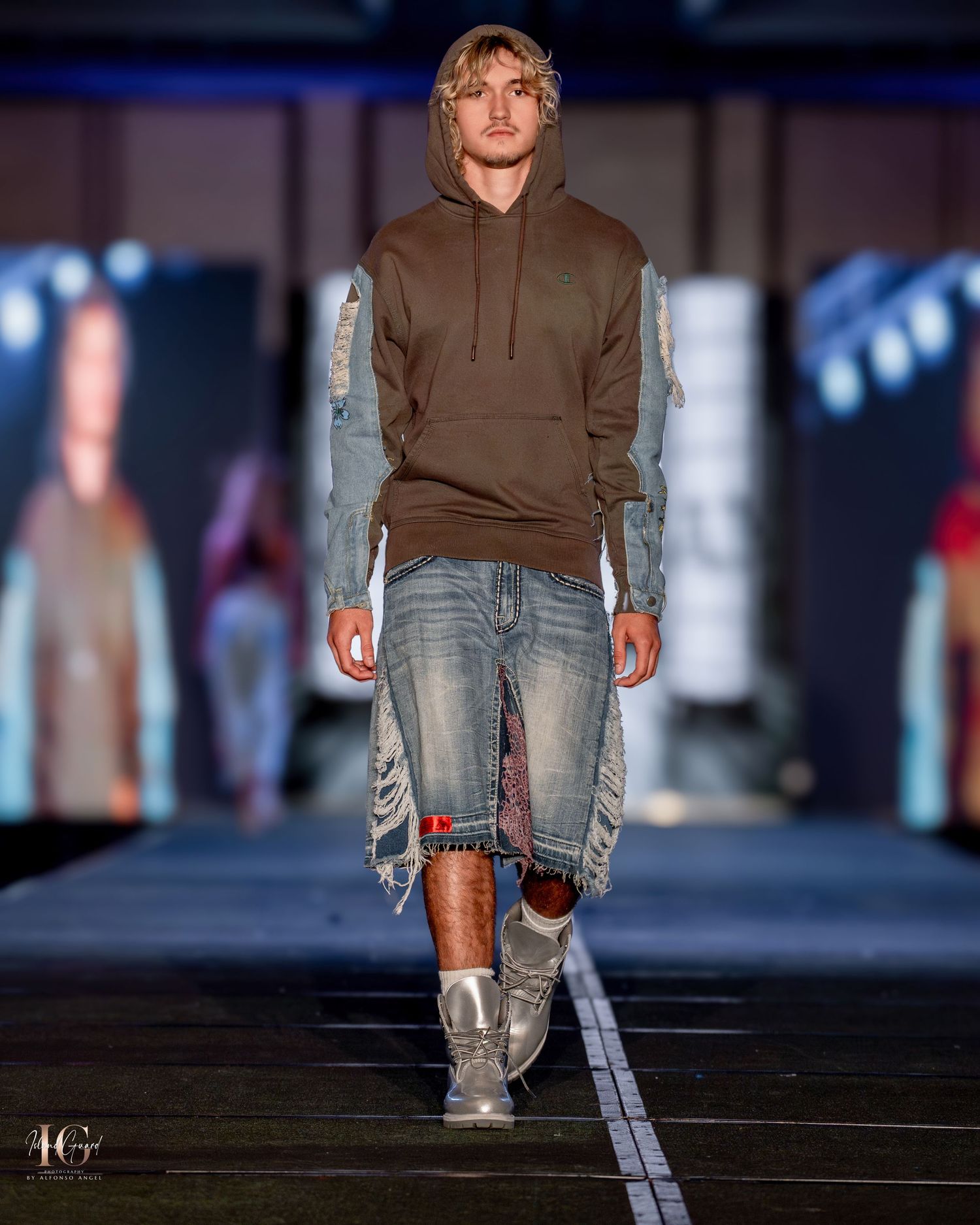 Model presents casual brown hoodie and distressed denim look on fashion runway.