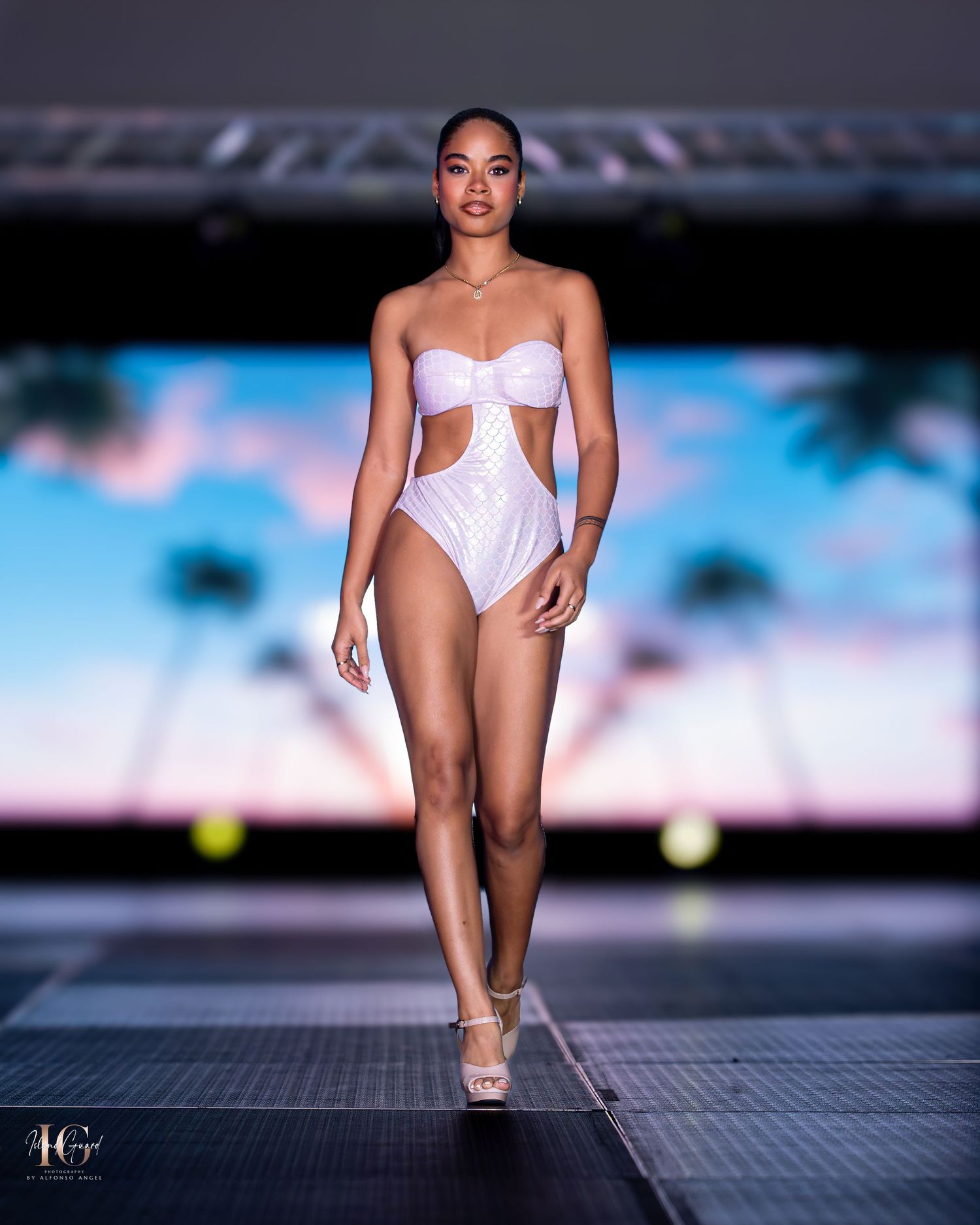 White swimwear collection displayed against blue backdrop on professional fashion runway.