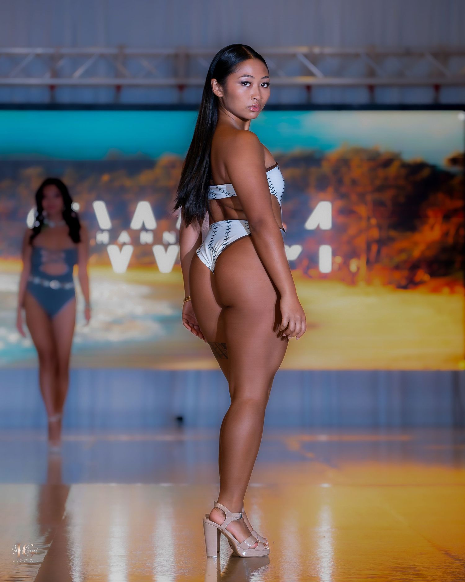 Models parade swimwear on a glossy runway with tropical beach backdrop.