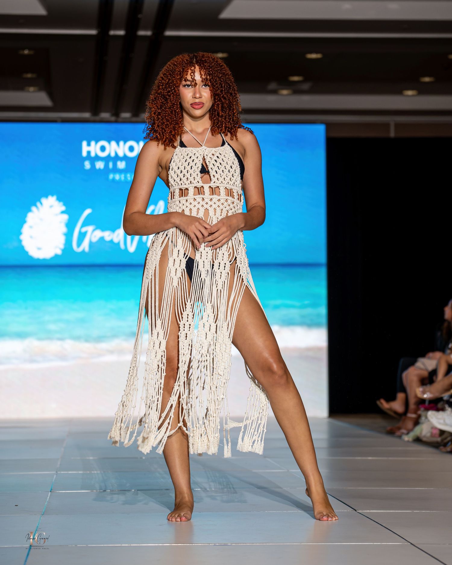 White macrame fringe swimwear design displayed on fashion runway with ocean backdrop.