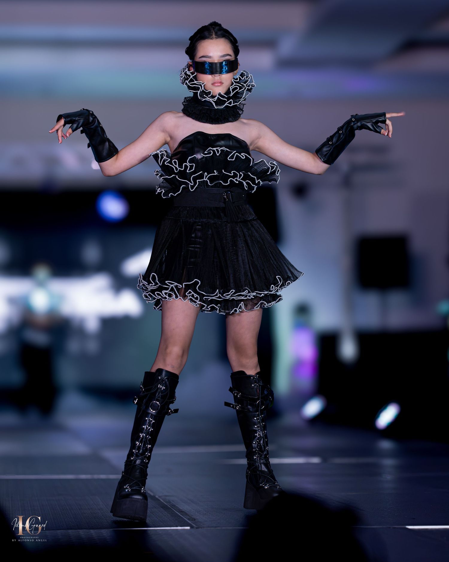 Dramatic black ruffled mini dress with knee-high boots on fashion runway.