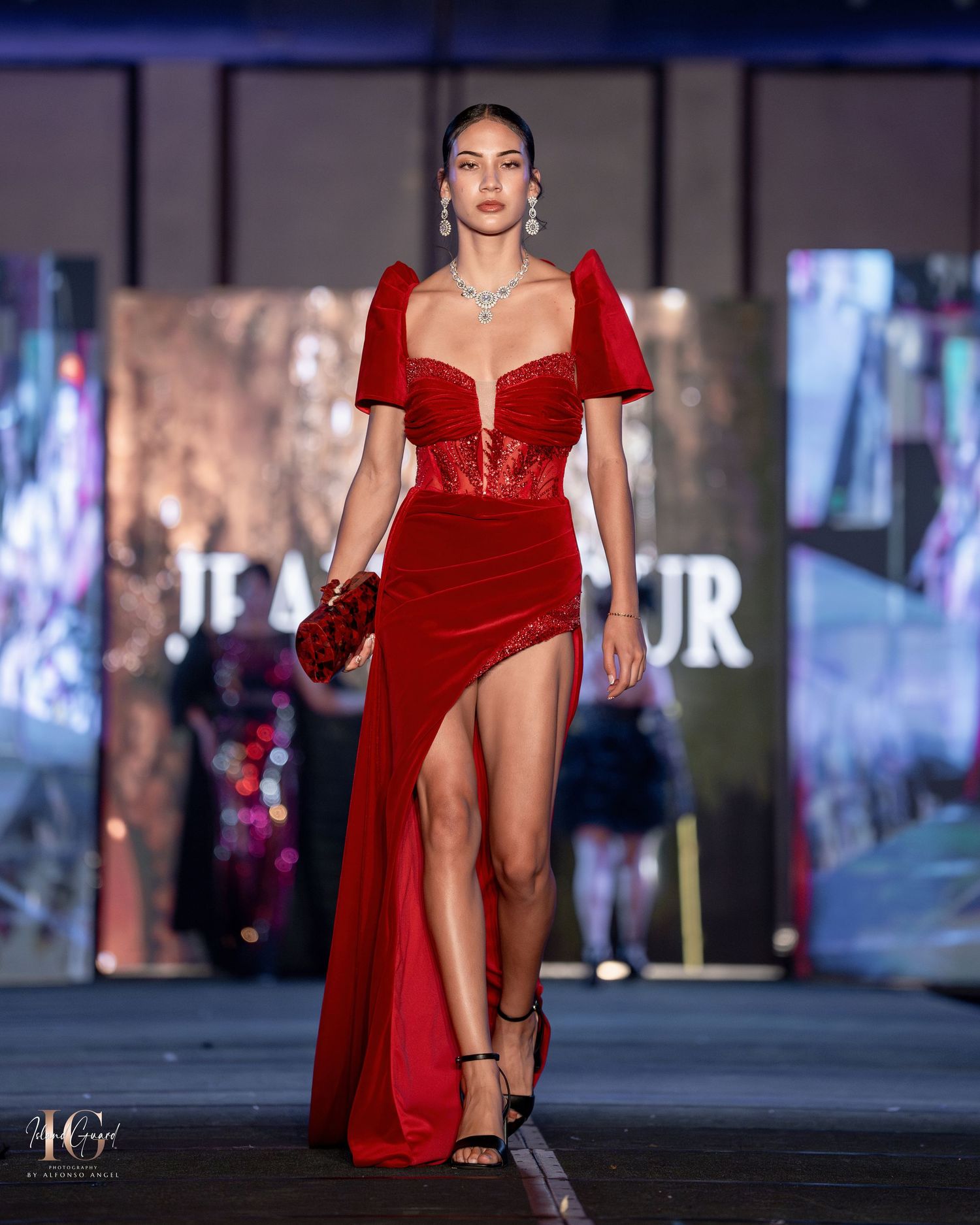 Elegant red velvet gown with sweetheart neckline and thigh-high slit on runway.