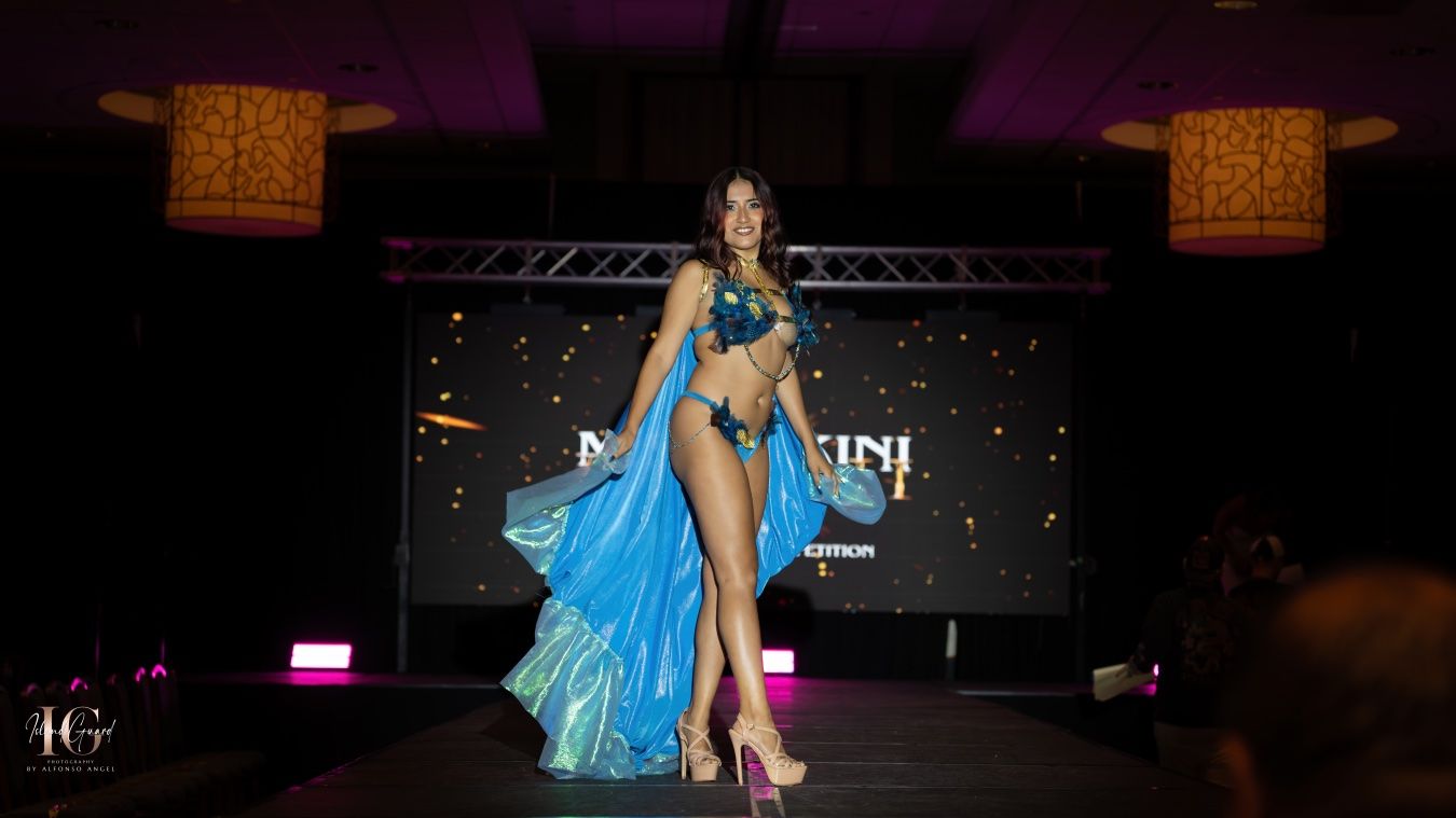A performer in a turquoise blue dance costume performs on stage under dramatic lighting.