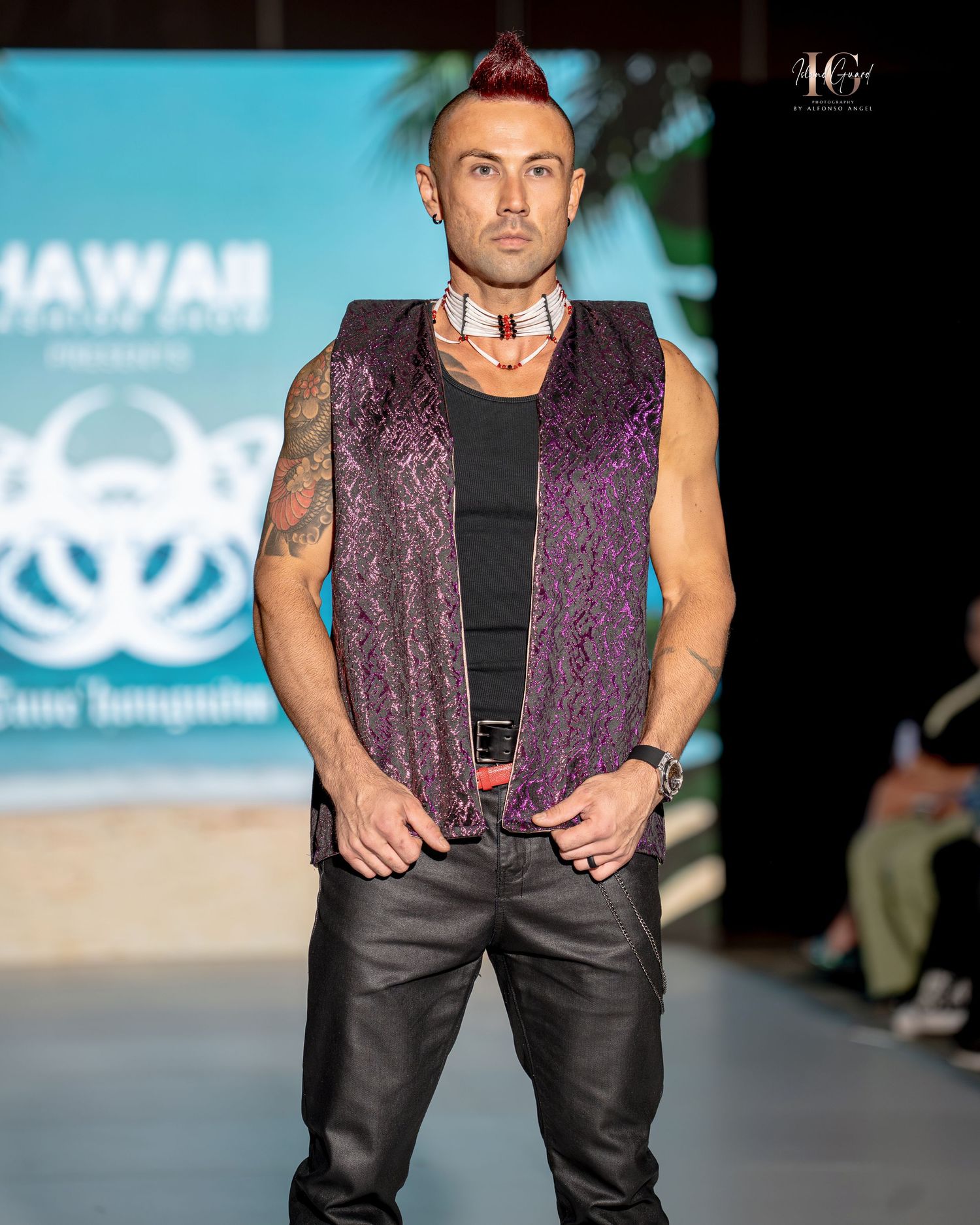Model walks runway in purple velvet vest with black pants during Hawaii fashion show.