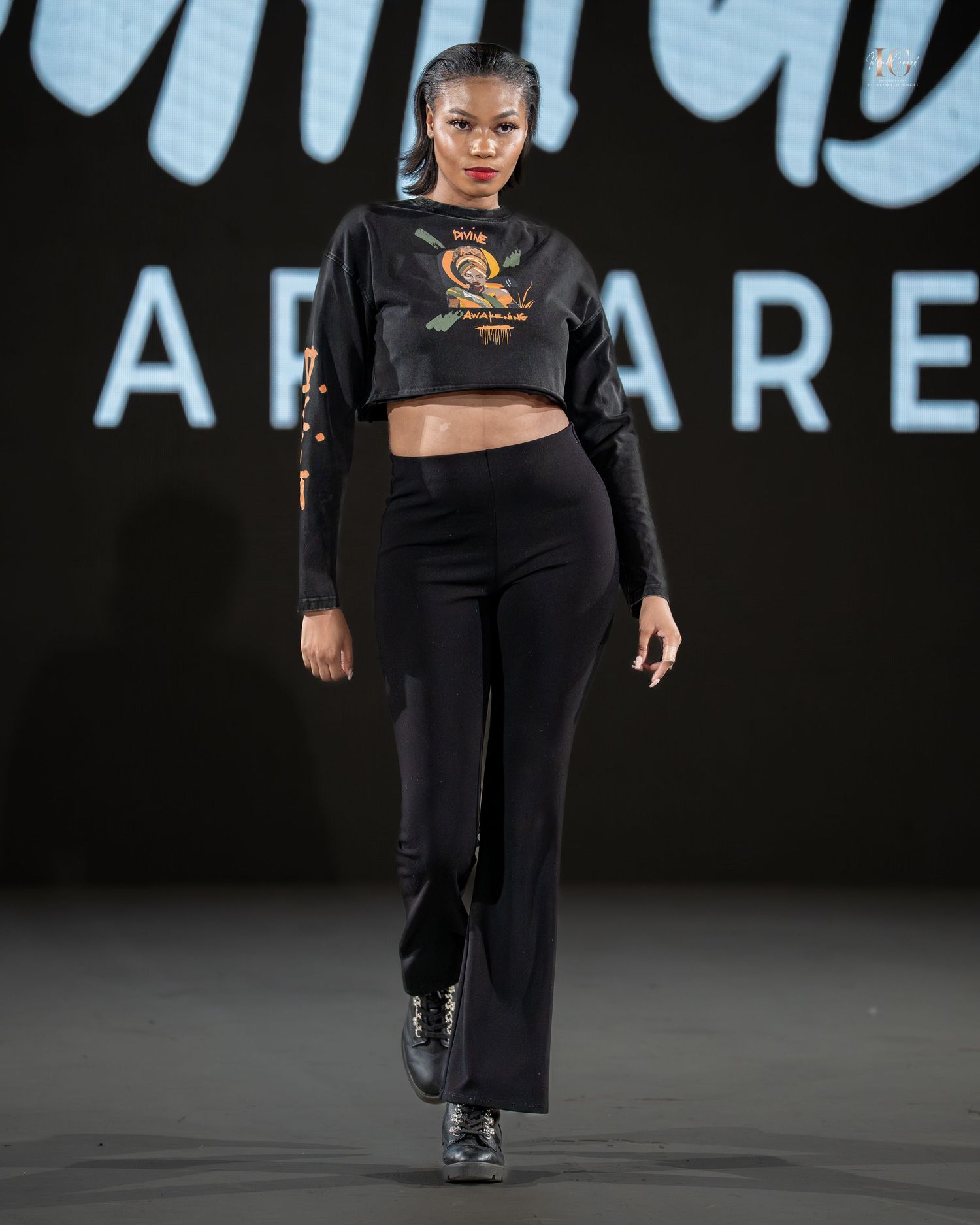 Model walks runway in black athleisure outfit with crop top and flared pants during fashion show.