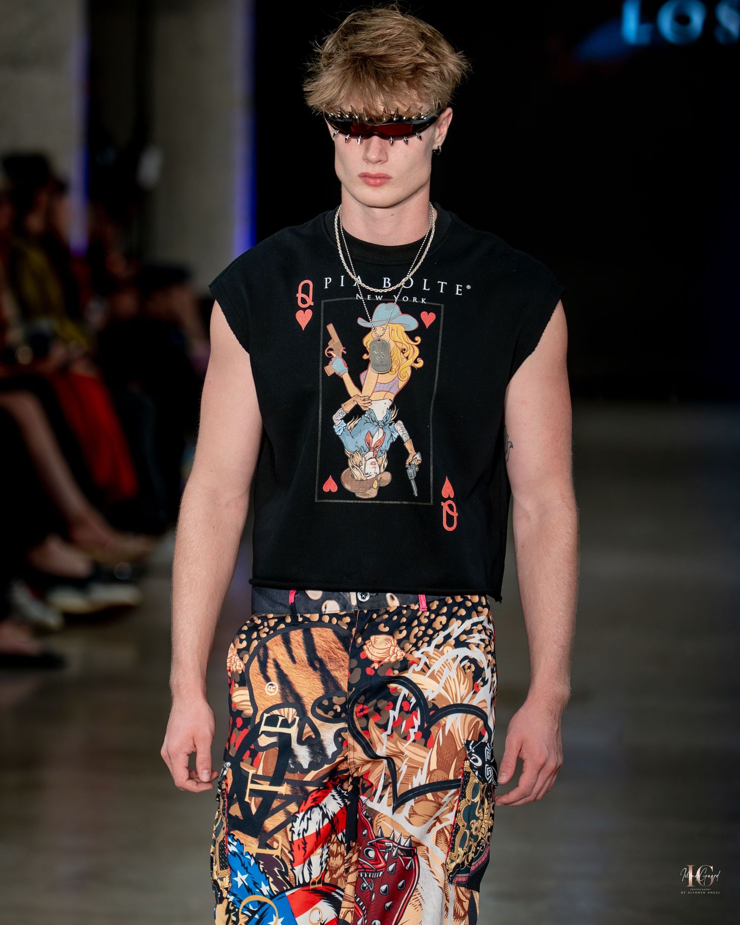 Fashion model walks runway wearing black graphic t-shirt and colorful comic book print shorts during fashion show.