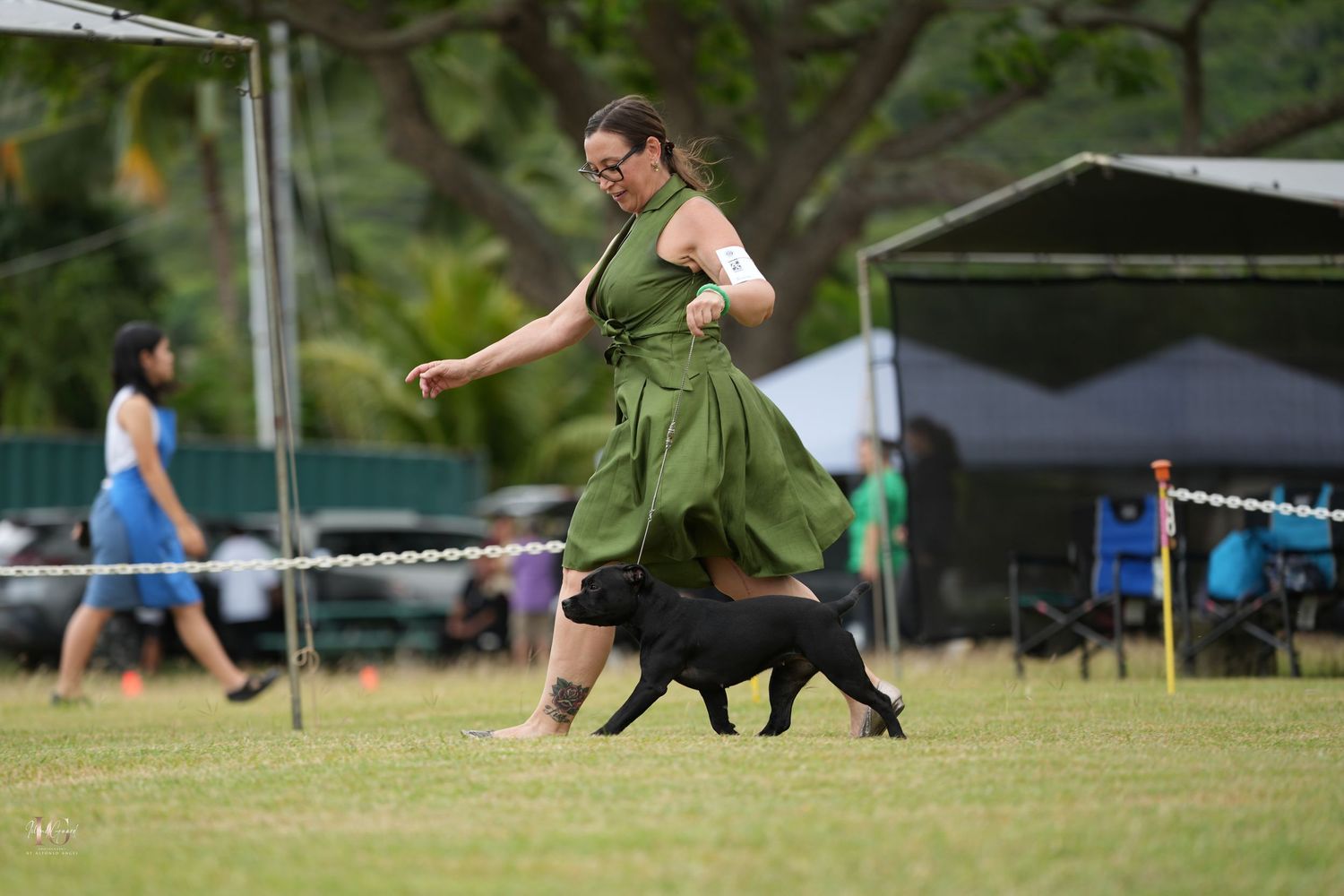 Handler and black dog performing together in an outdoor agility competition on grassy field.