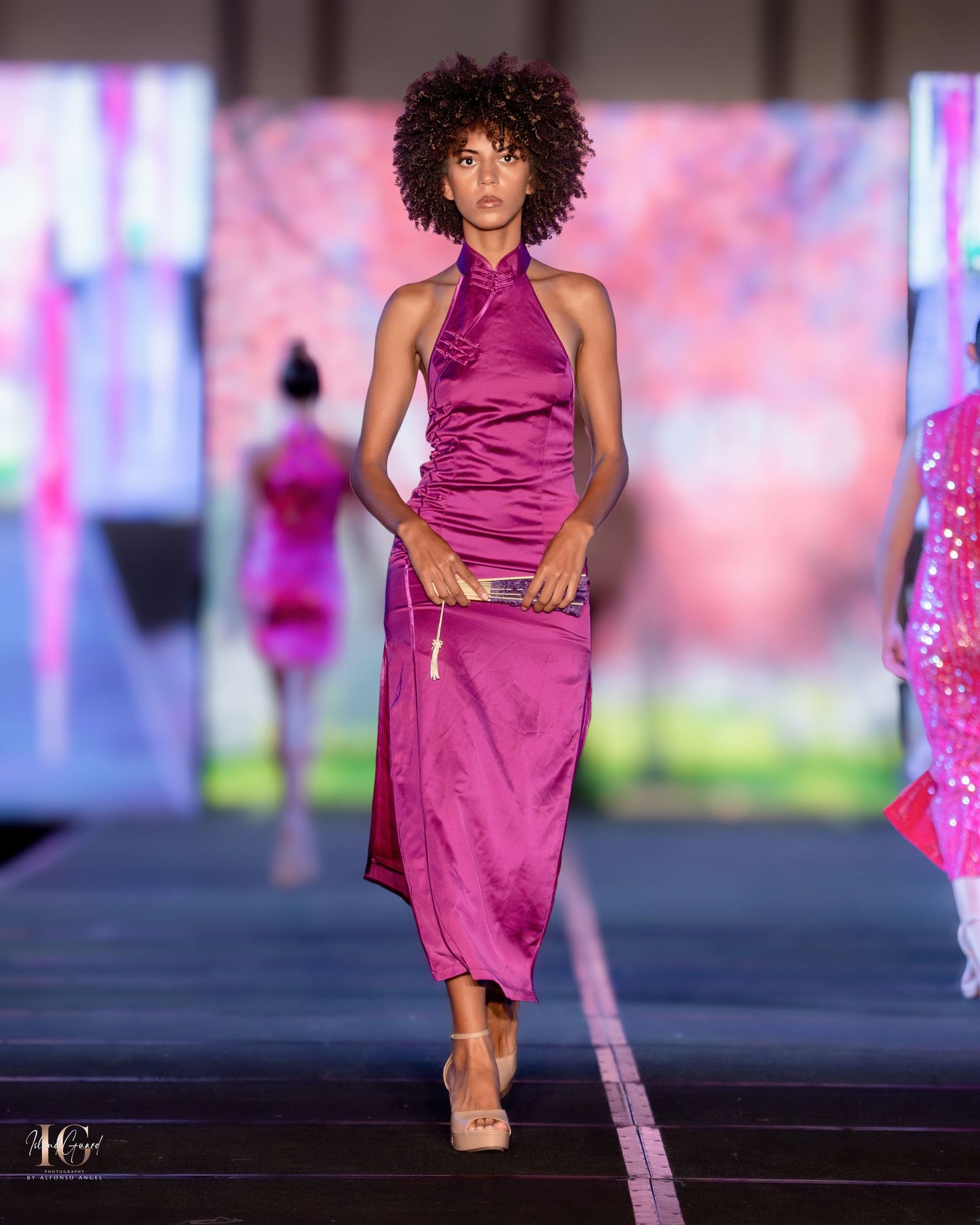 Fashion model walks runway in magenta silk halter dress with fitted silhouette and midi length.