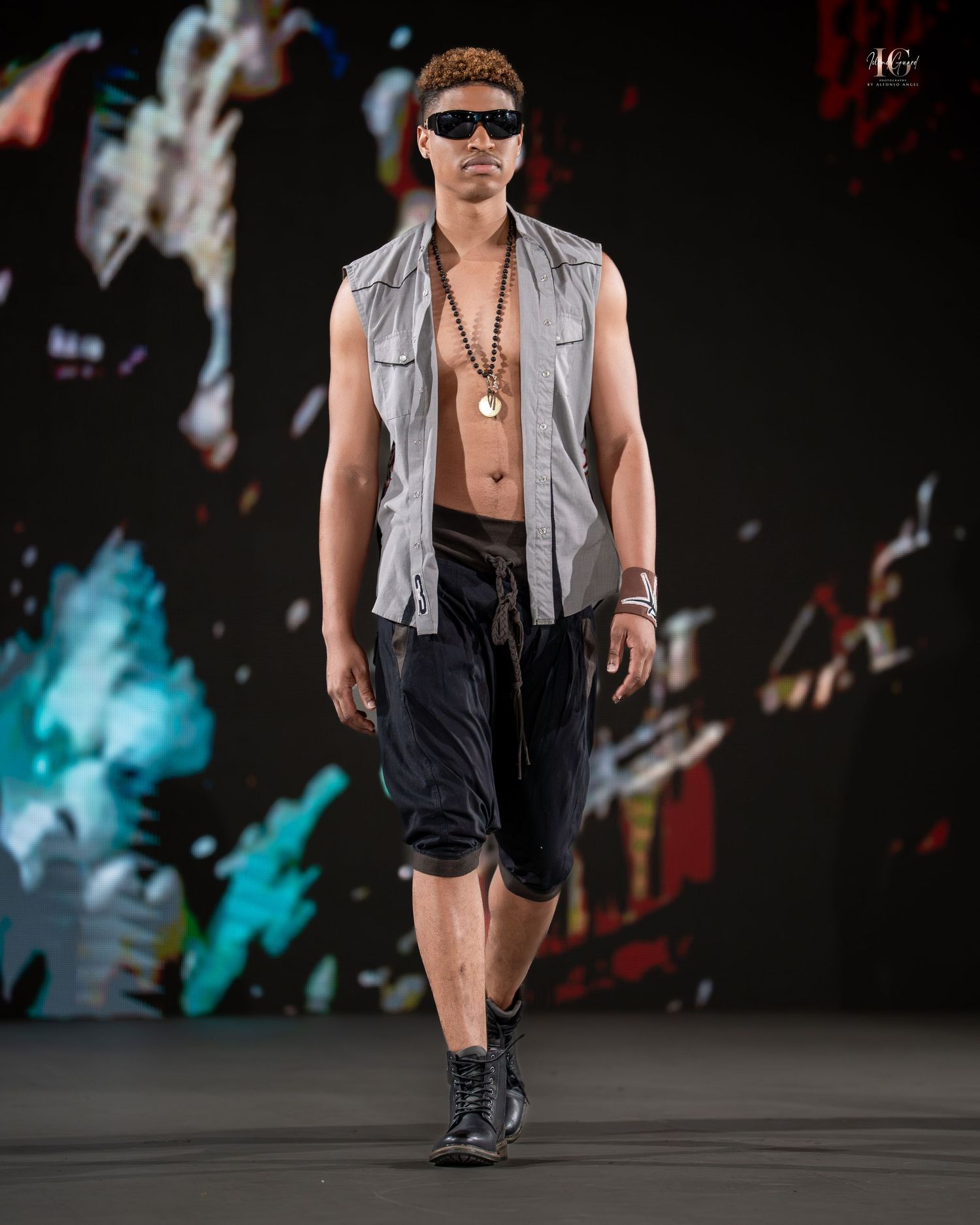 A model walks the runway in a sleeveless gray vest, black shorts and boots at a fashion show.