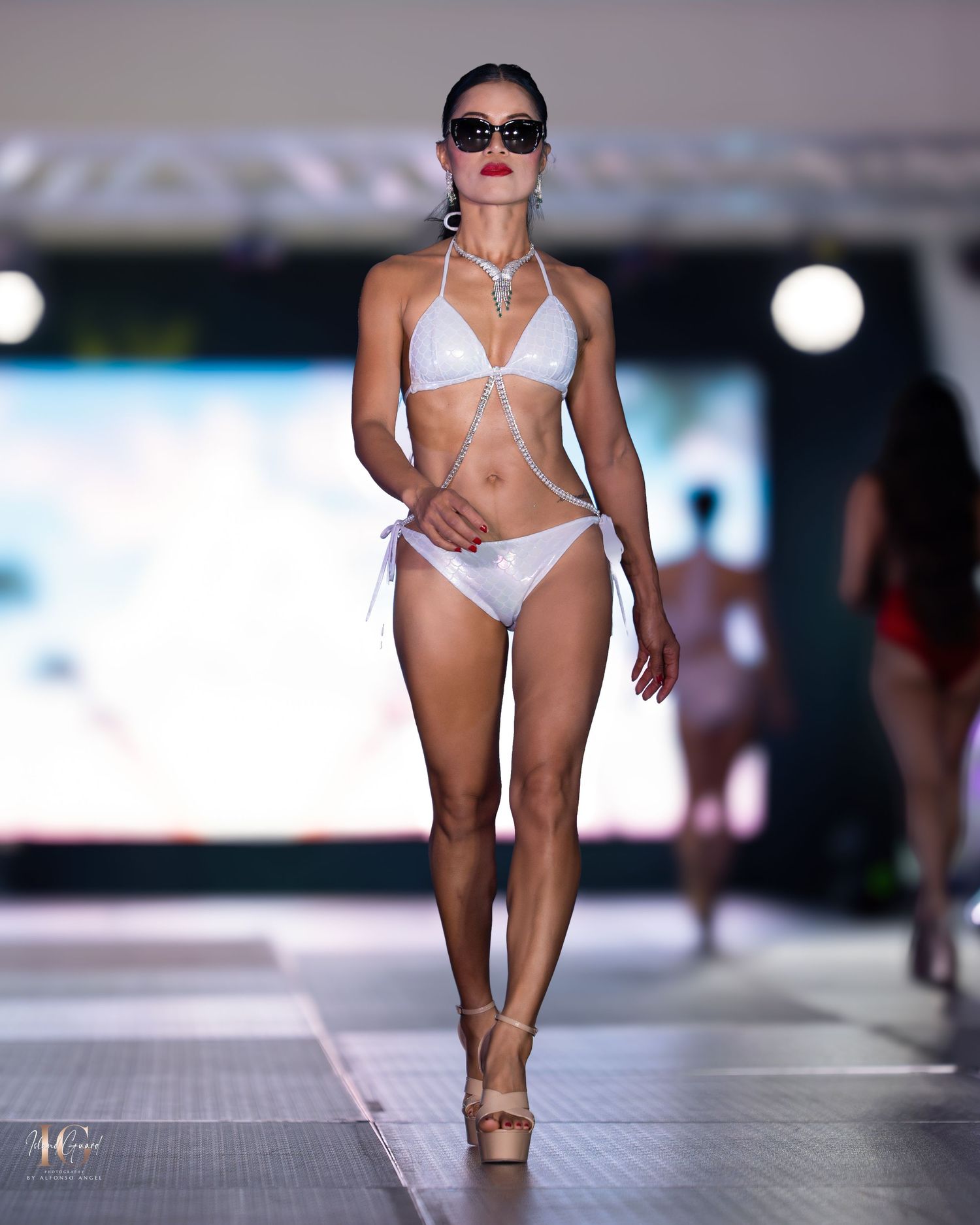 Swimwear model presents white bikini and platform heels on catwalk.