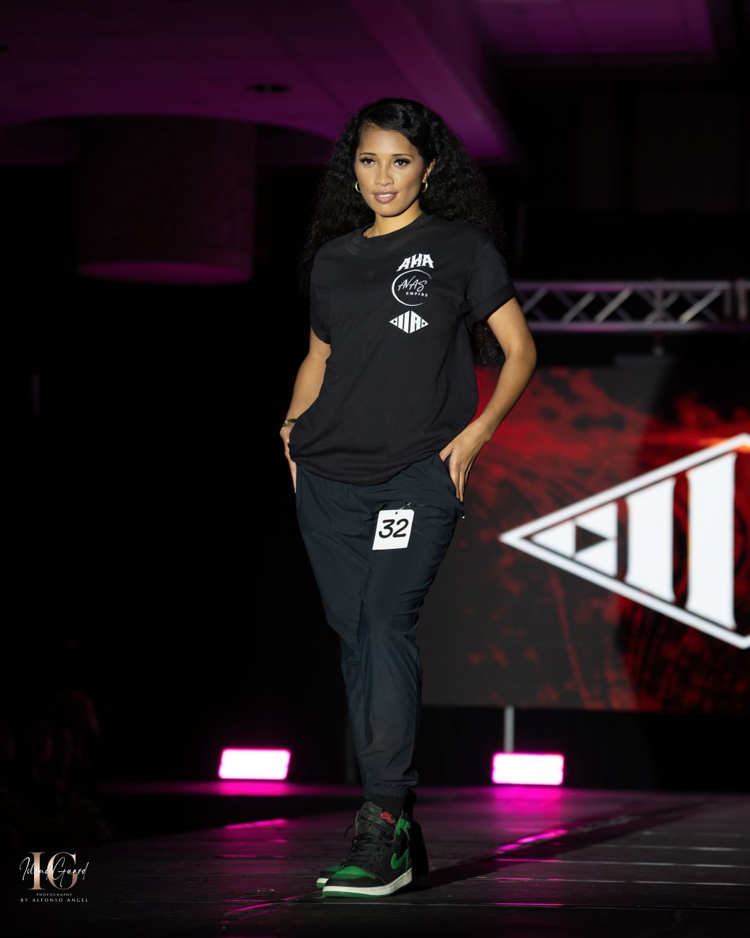 Model showcases sporty black outfit with graphics on illuminated fashion runway.