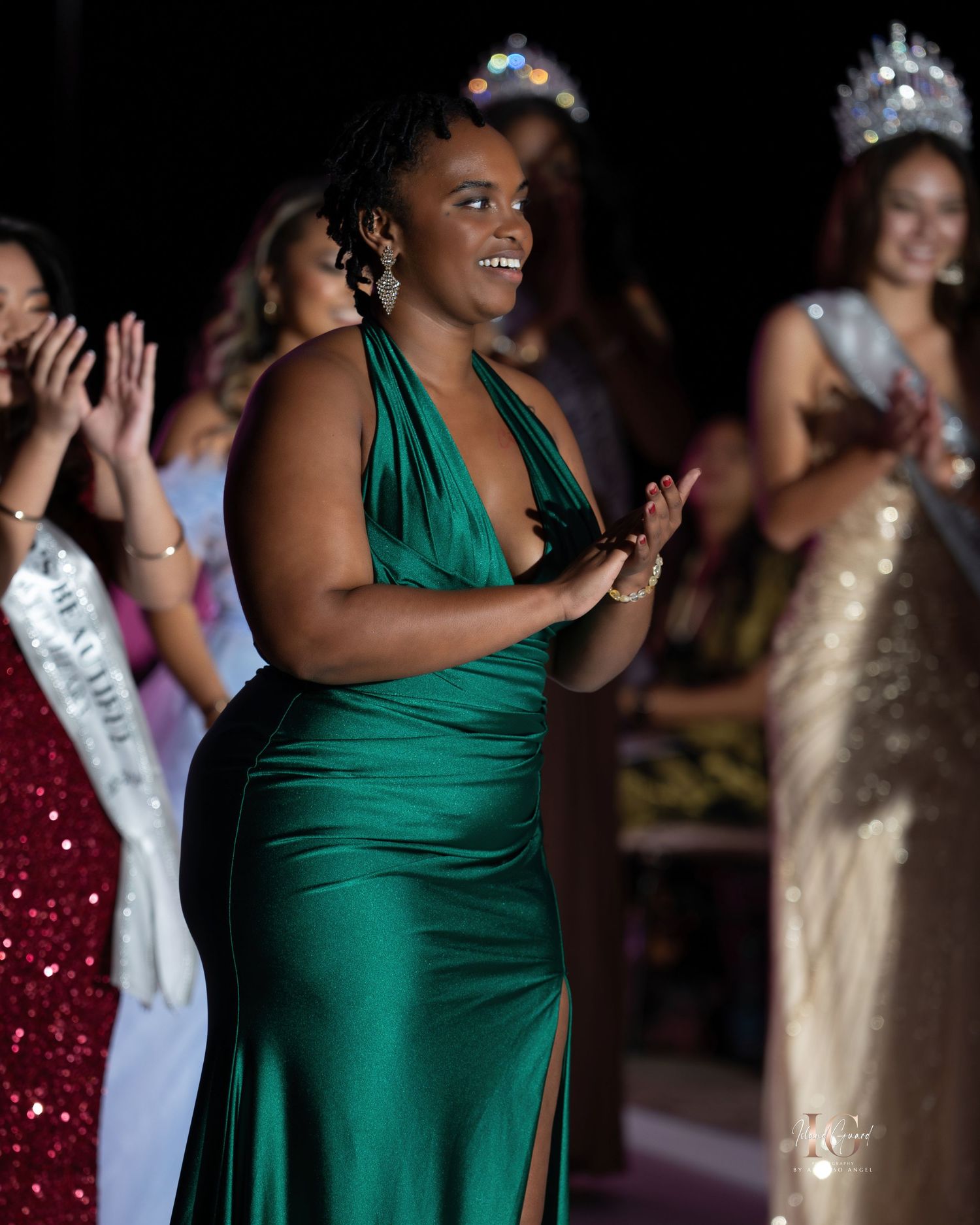 A contestant in a green evening gown stands on stage during a pageant competition.