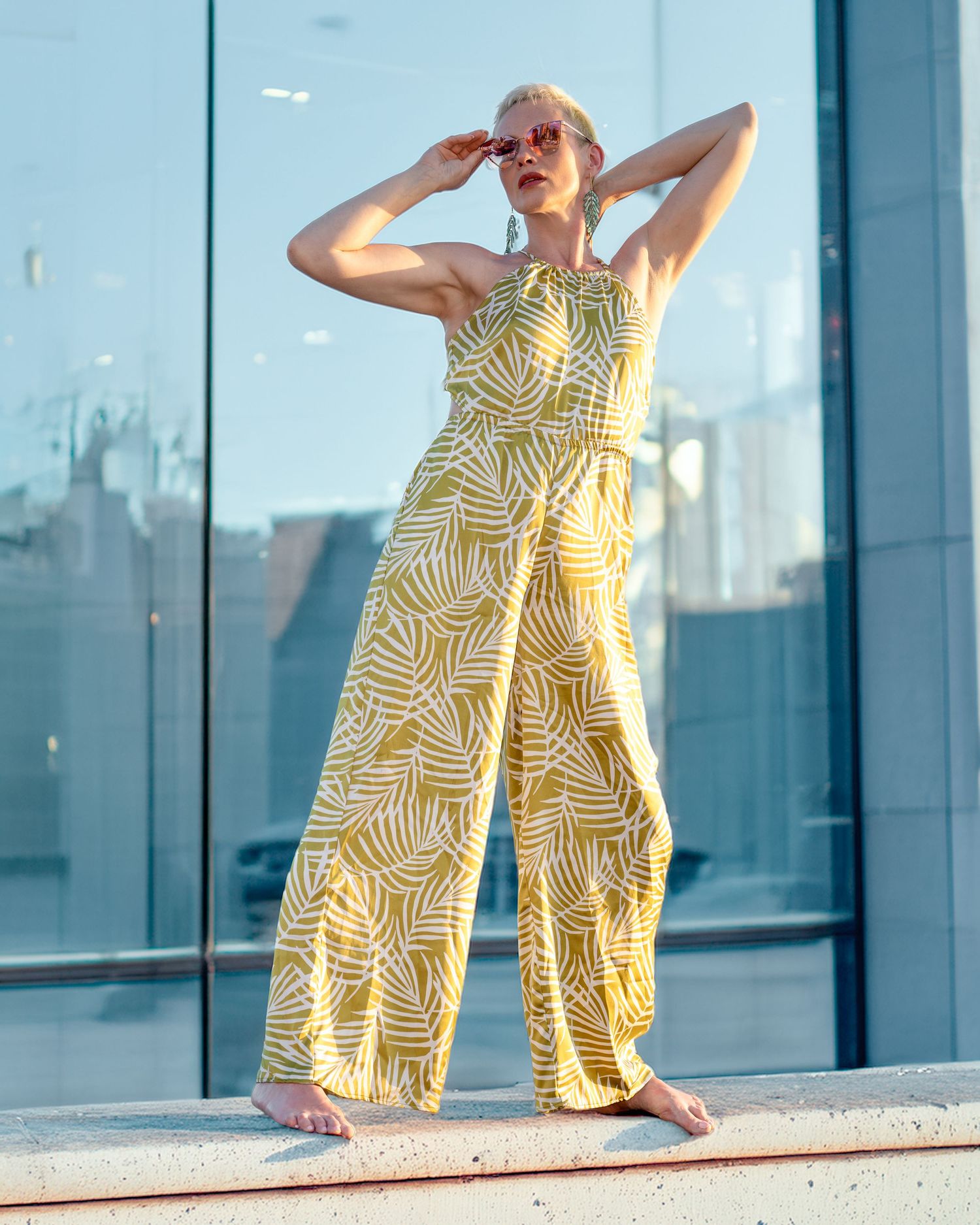 Fashionable yellow jumpsuit with geometric patterns shown in three poses against a modern glass building exterior.