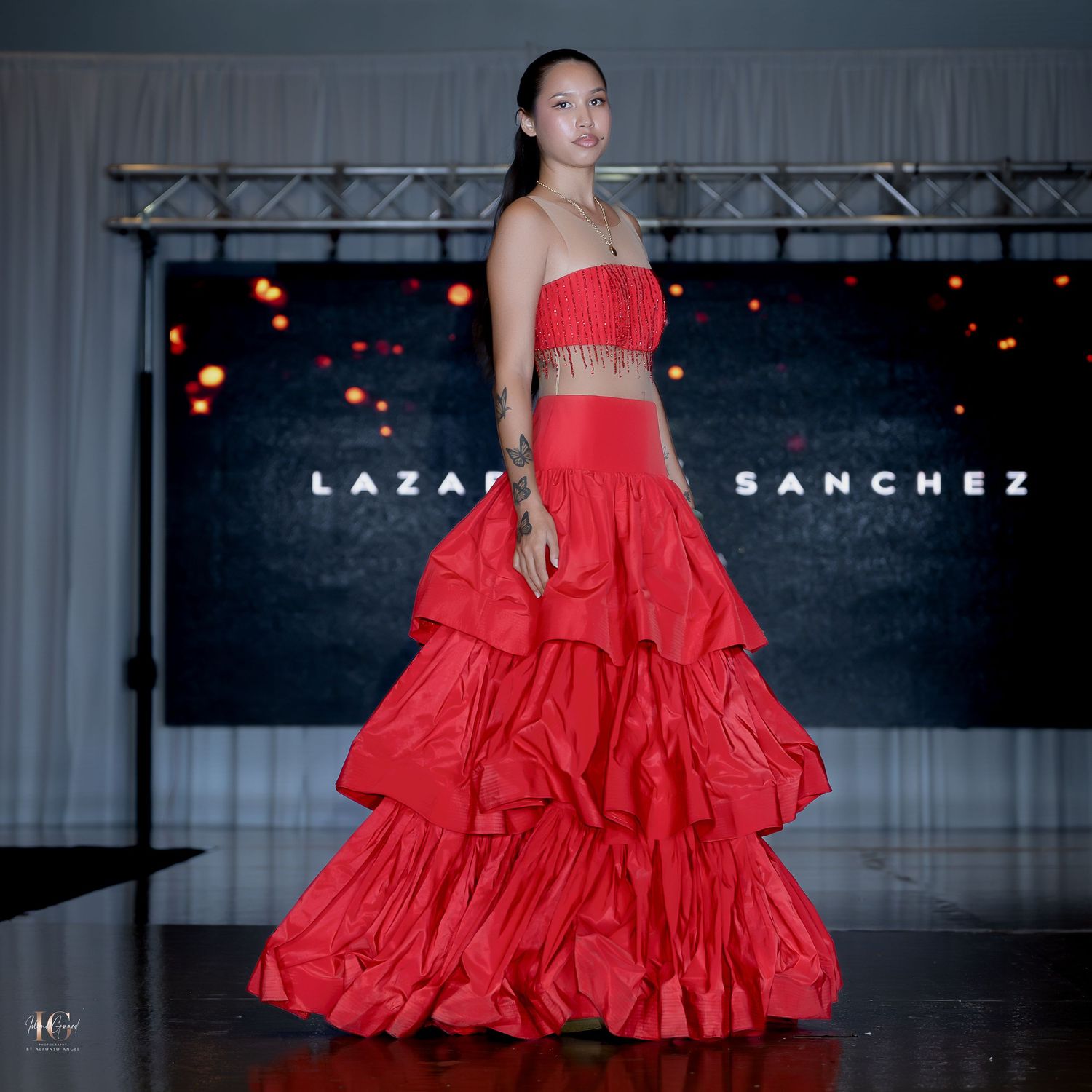 Models present dramatic red formal gowns on dimly lit fashion runway.