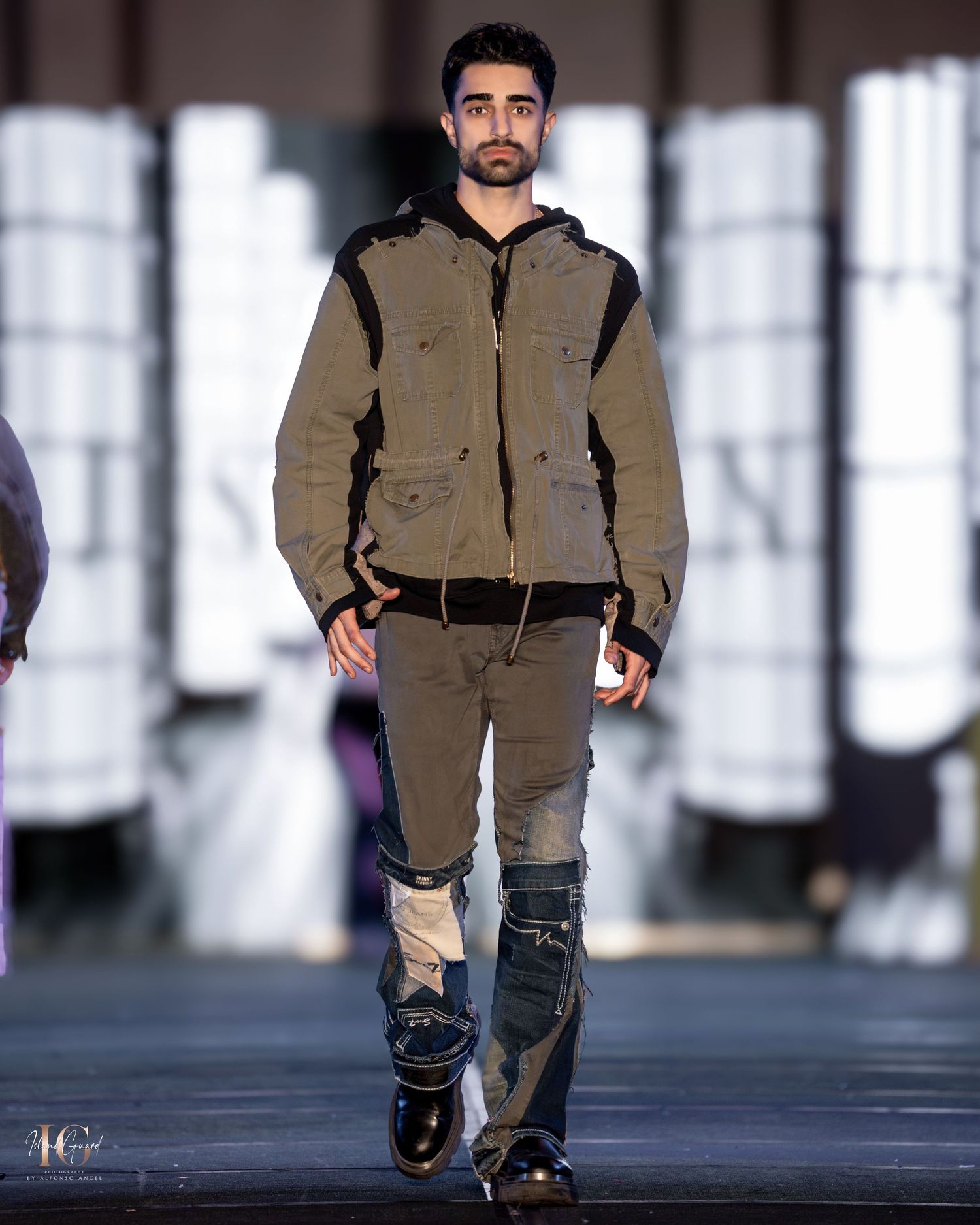 Model showcases urban streetwear with brown hooded jacket and utility pants on modern runway.