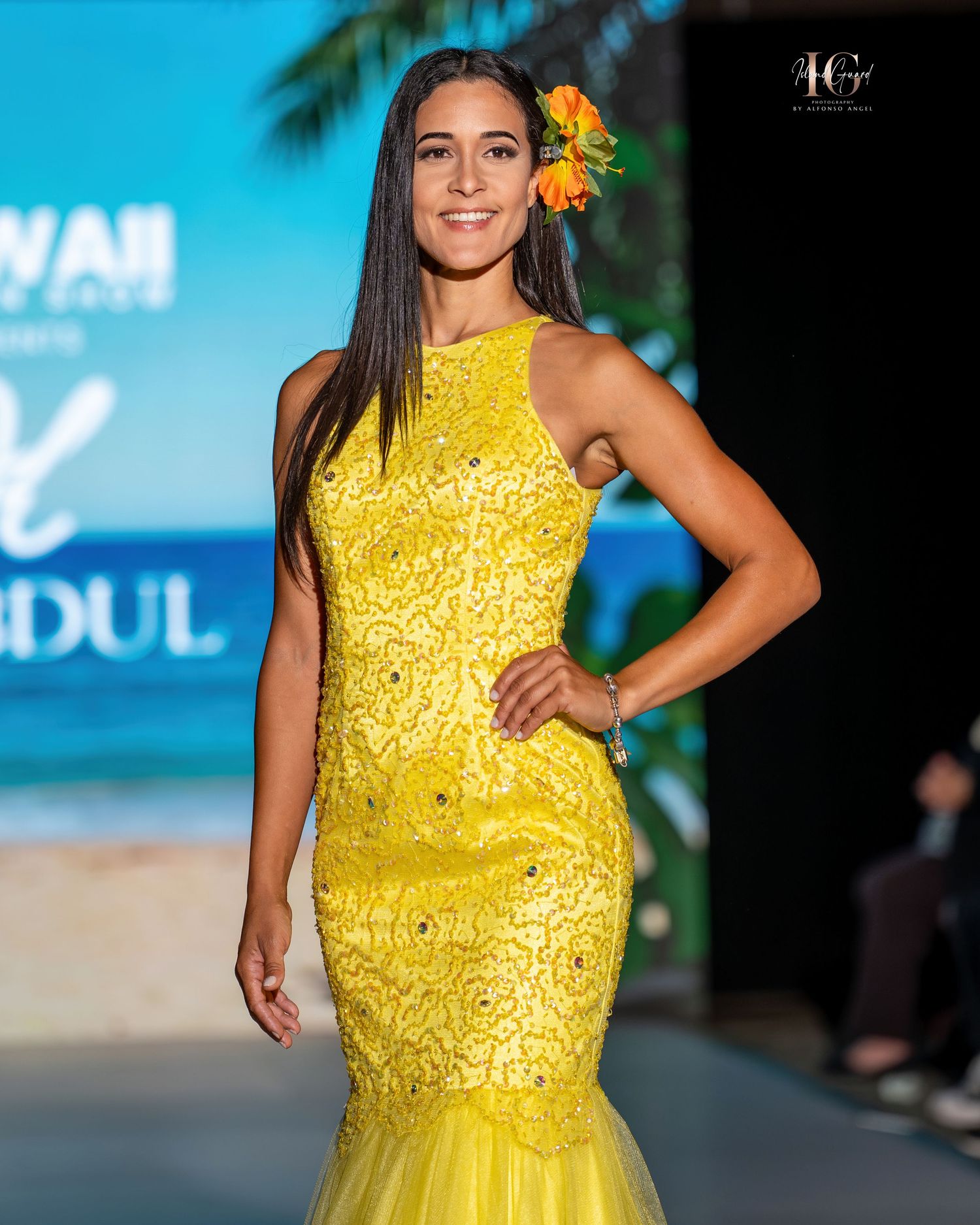 Model walks runway in bright yellow sequined evening gown during fashion show.