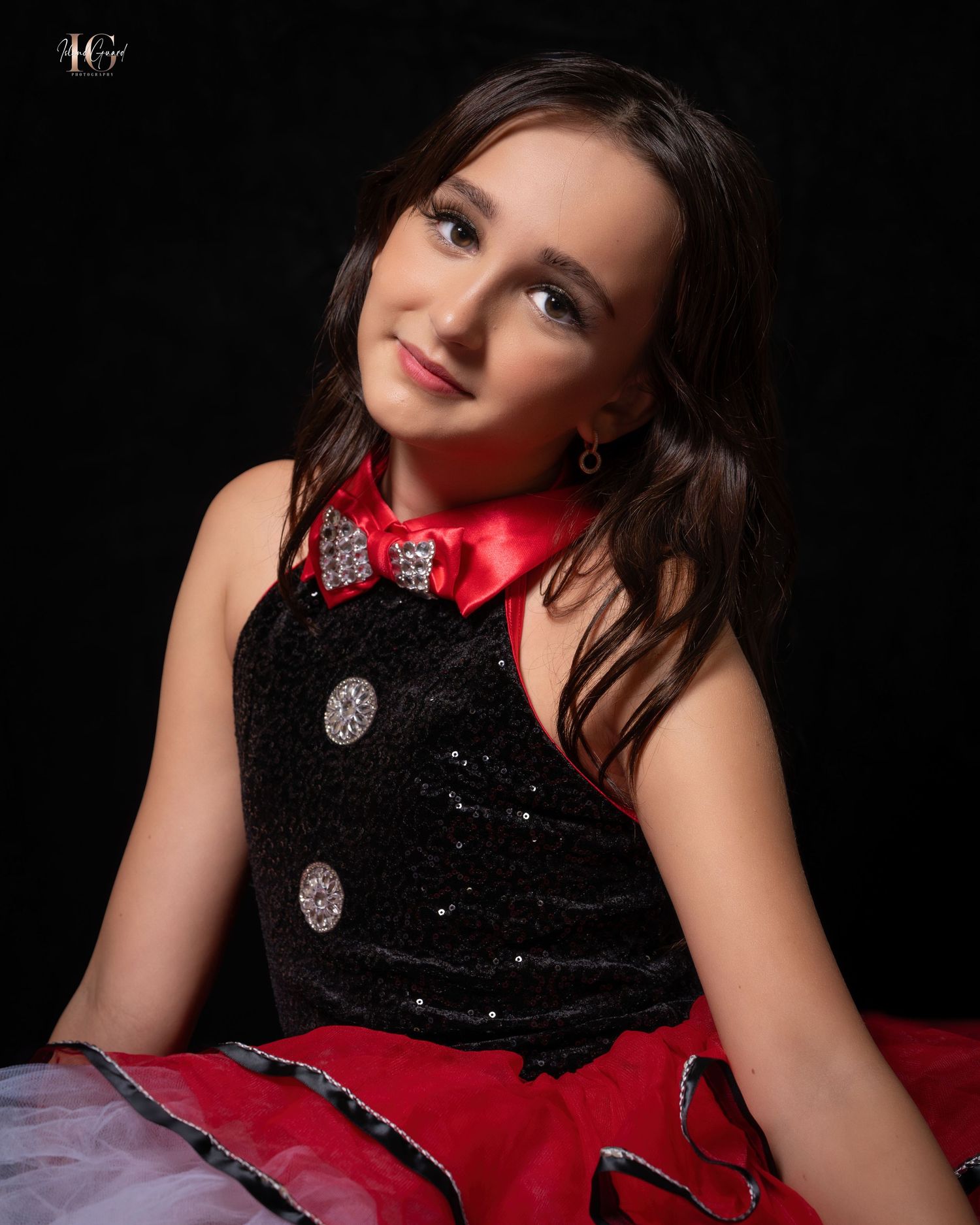Child in a sparkly black and red dress poses elegantly against dark background during portrait session.