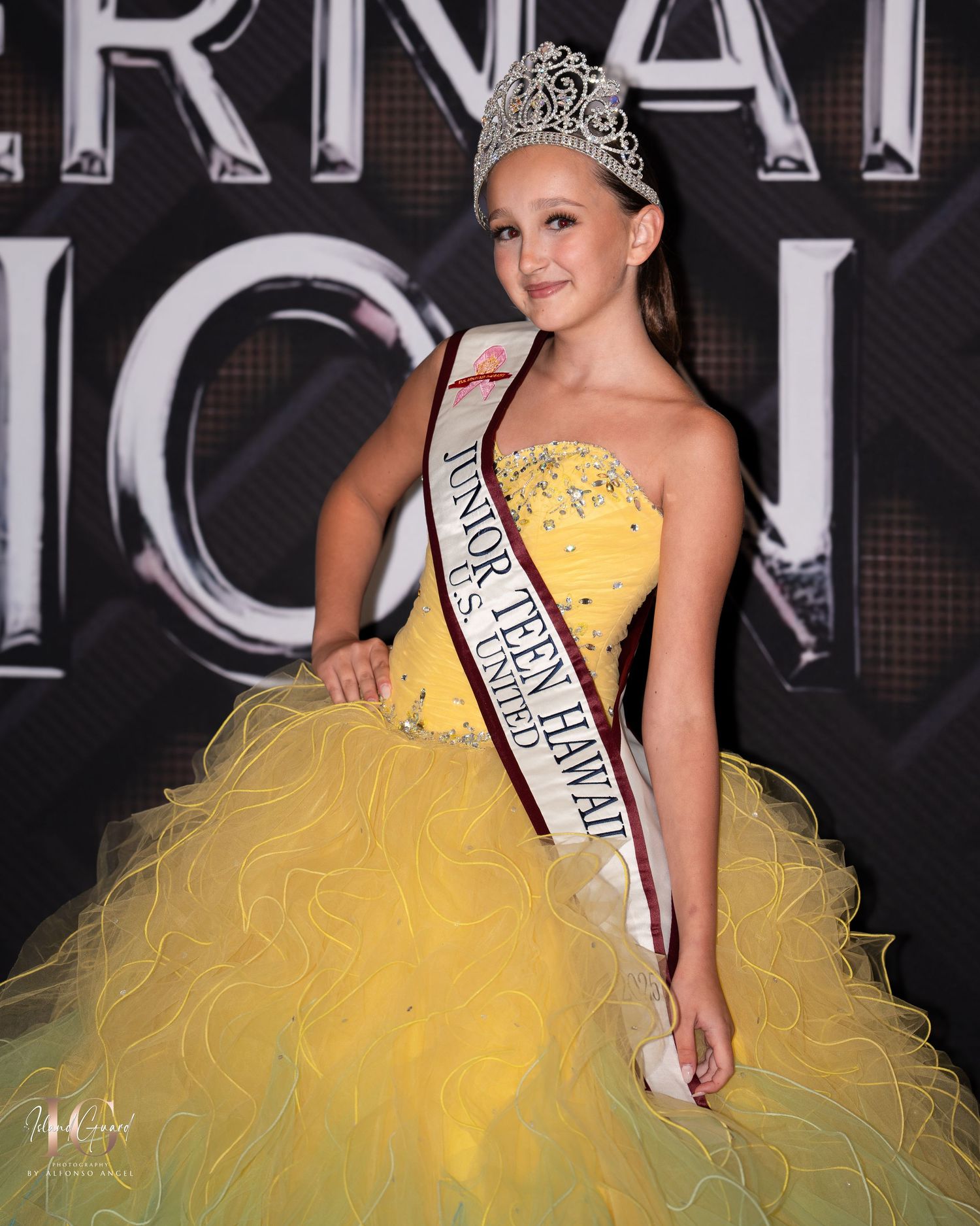 A pageant contestant wearing a sparkling yellow ball gown and tiara poses against a dark backdrop with elegant signage.