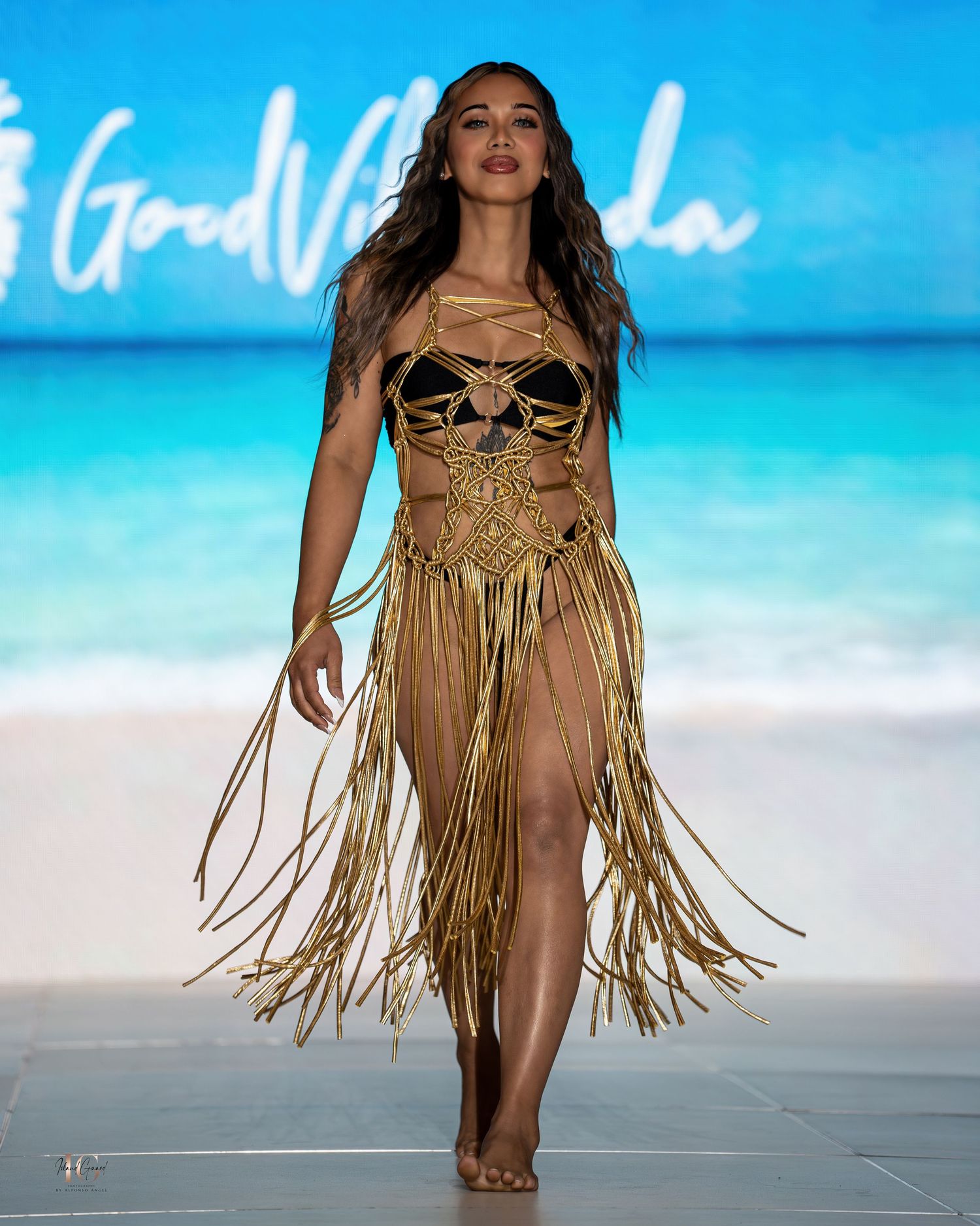 Tan fringe swimwear design presented on catwalk with beach backdrop at swim fashion show.