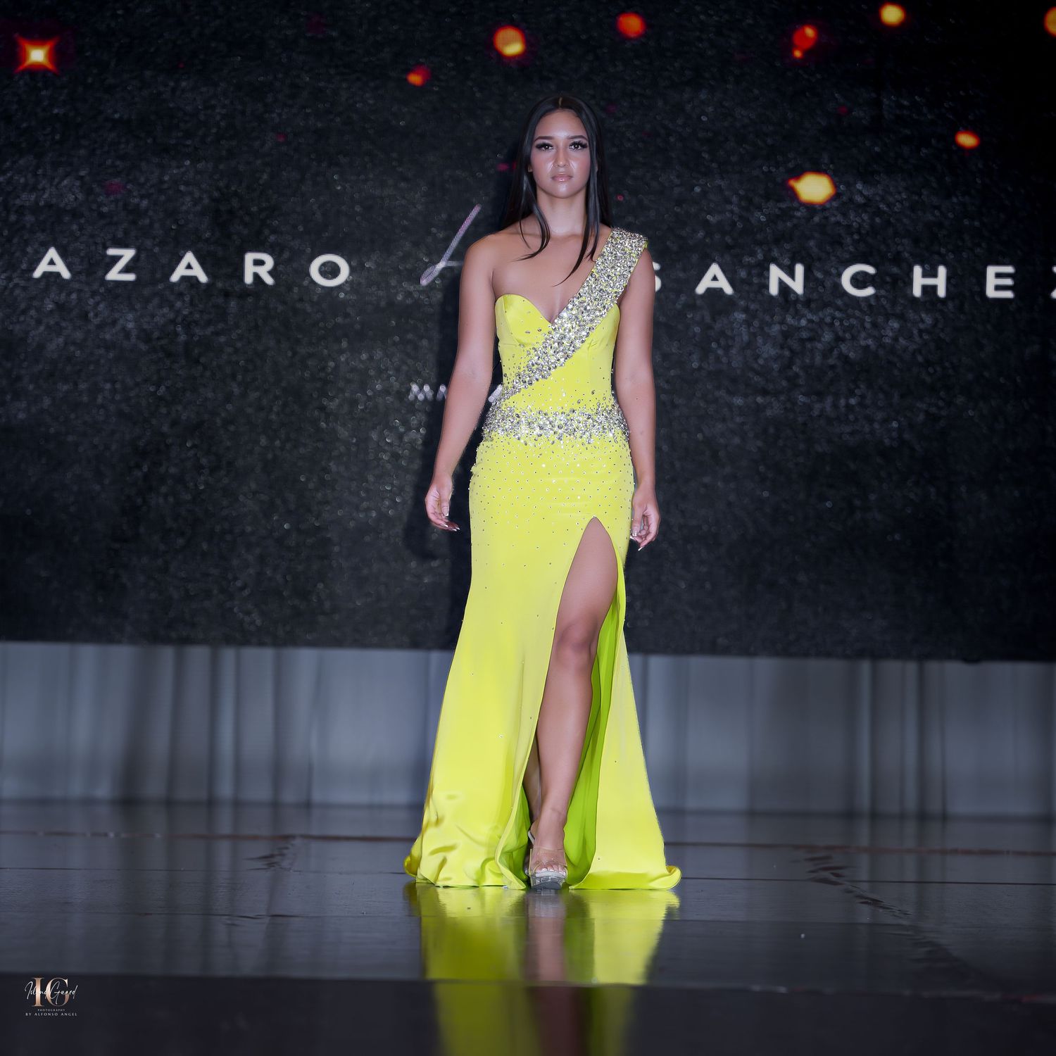 Model walks runway in yellow evening gown with crystal embellishments and thigh-high slit.