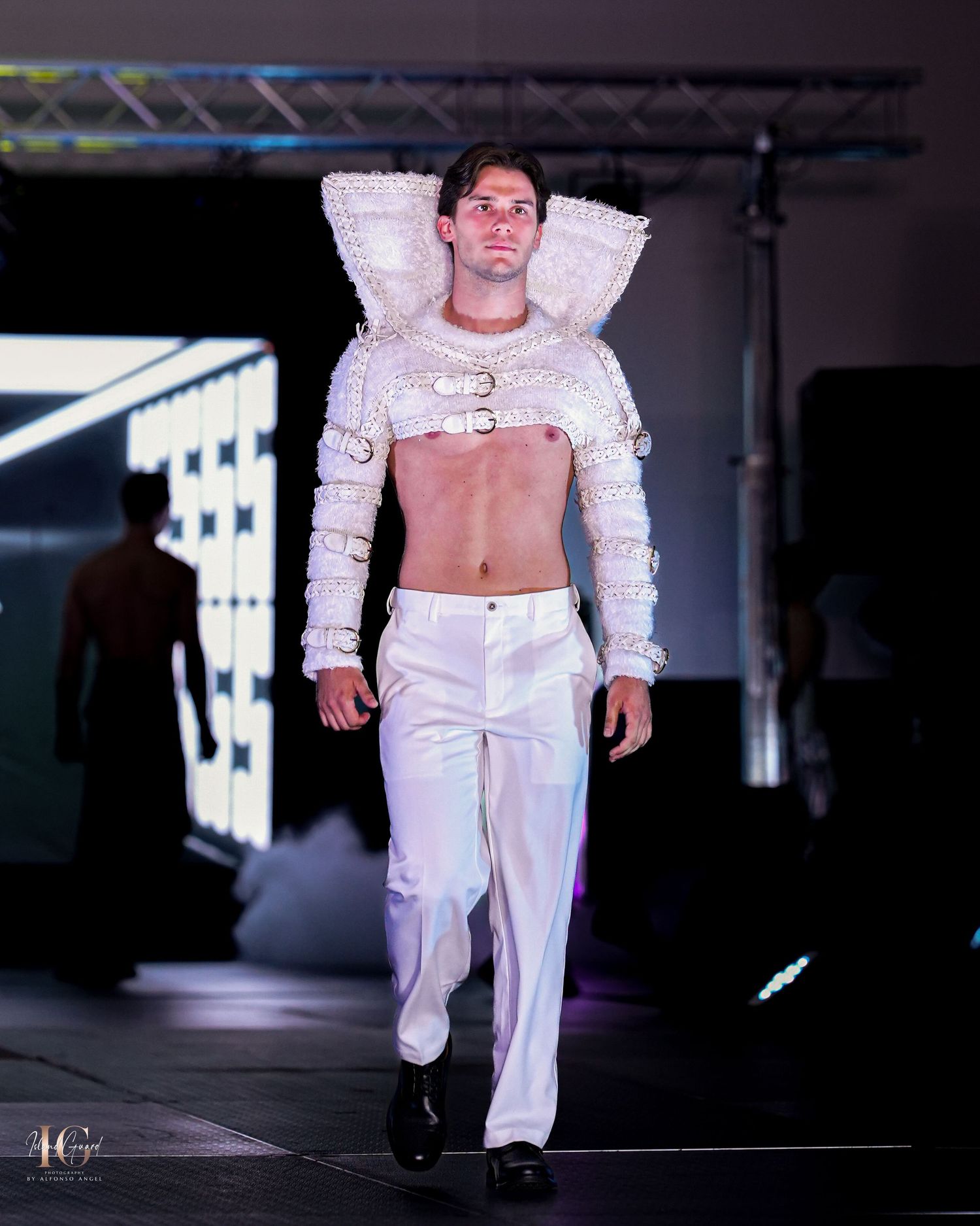 Model wearing structured white cropped jacket with dramatic shoulders and white pants on runway.