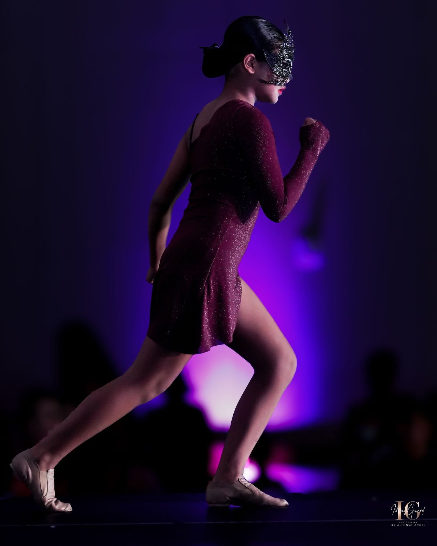 Artistic silhouette of performer in burgundy dress against purple stage lighting.
