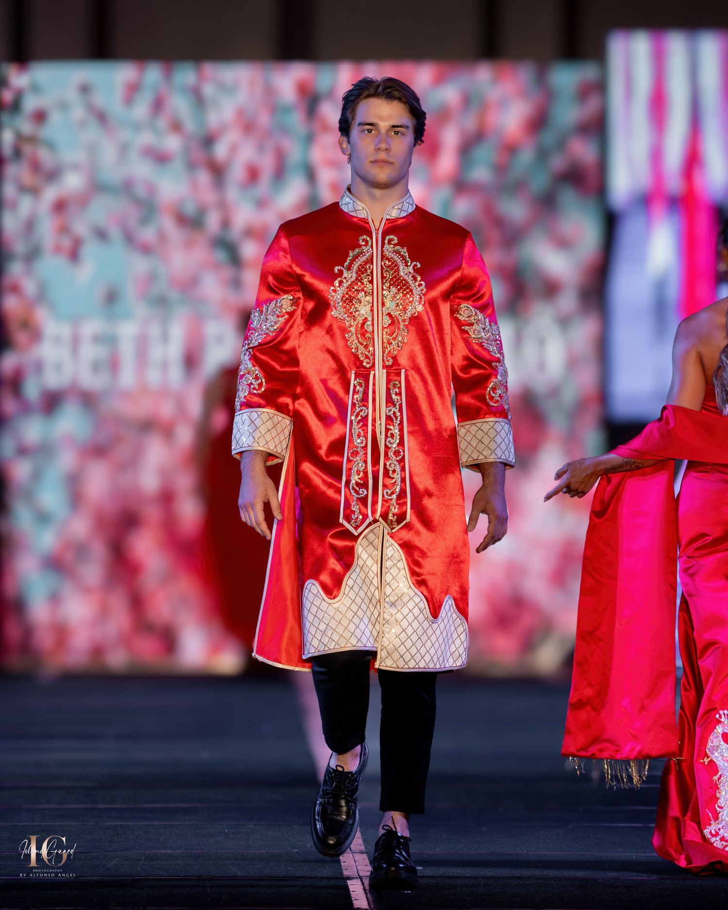 Model presents traditional red Asian-inspired jacket with gold embroidery on fashion runway.