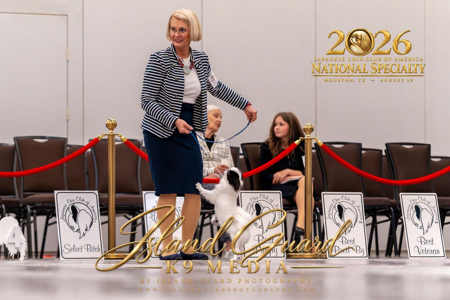 Handler presents a dog at the 2026 National Specialty dog show, with red rope barriers and audience in background.