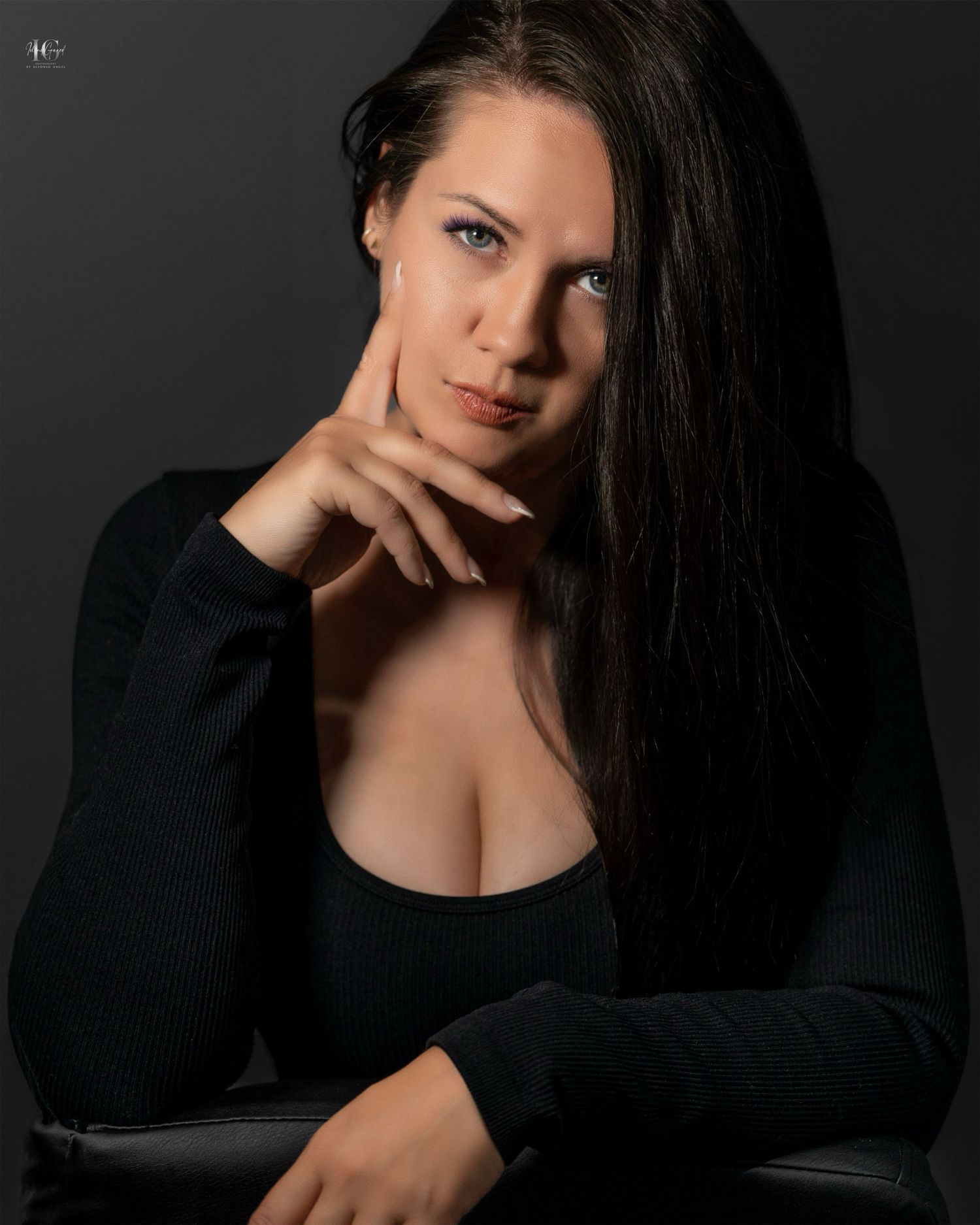 Moody portrait in black sweater with dramatic lighting against dark background.