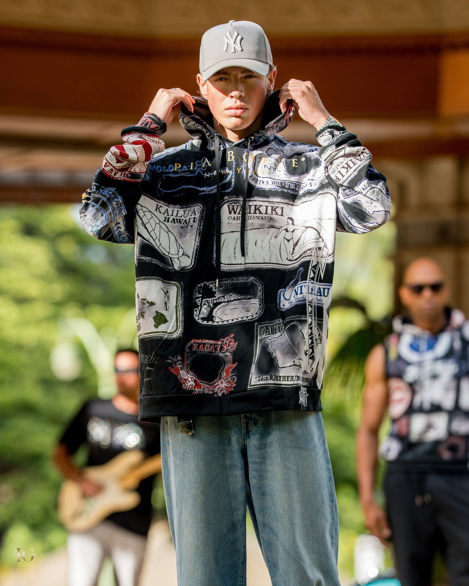 Person wearing a black and white graphic jacket with jeans stands in an outdoor setting.