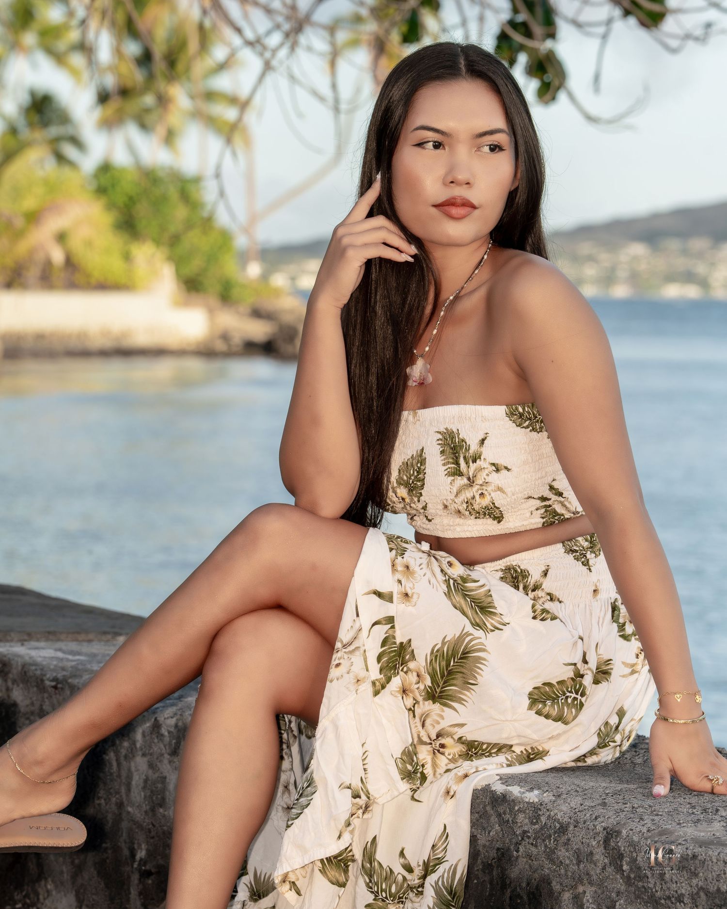 A woman in a floral sundress poses outdoors near a waterfront on a sunny day.