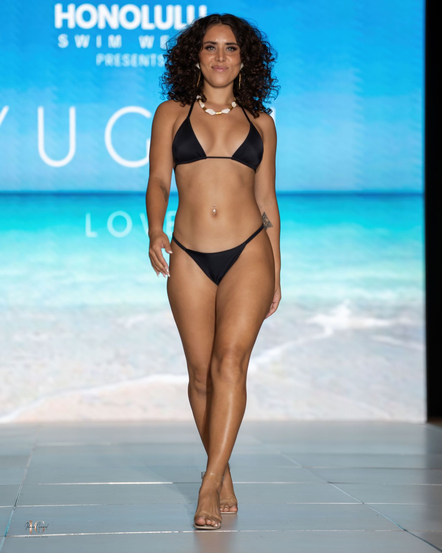 Model walks runway in classic black triangle bikini at Honolulu Swim Week.