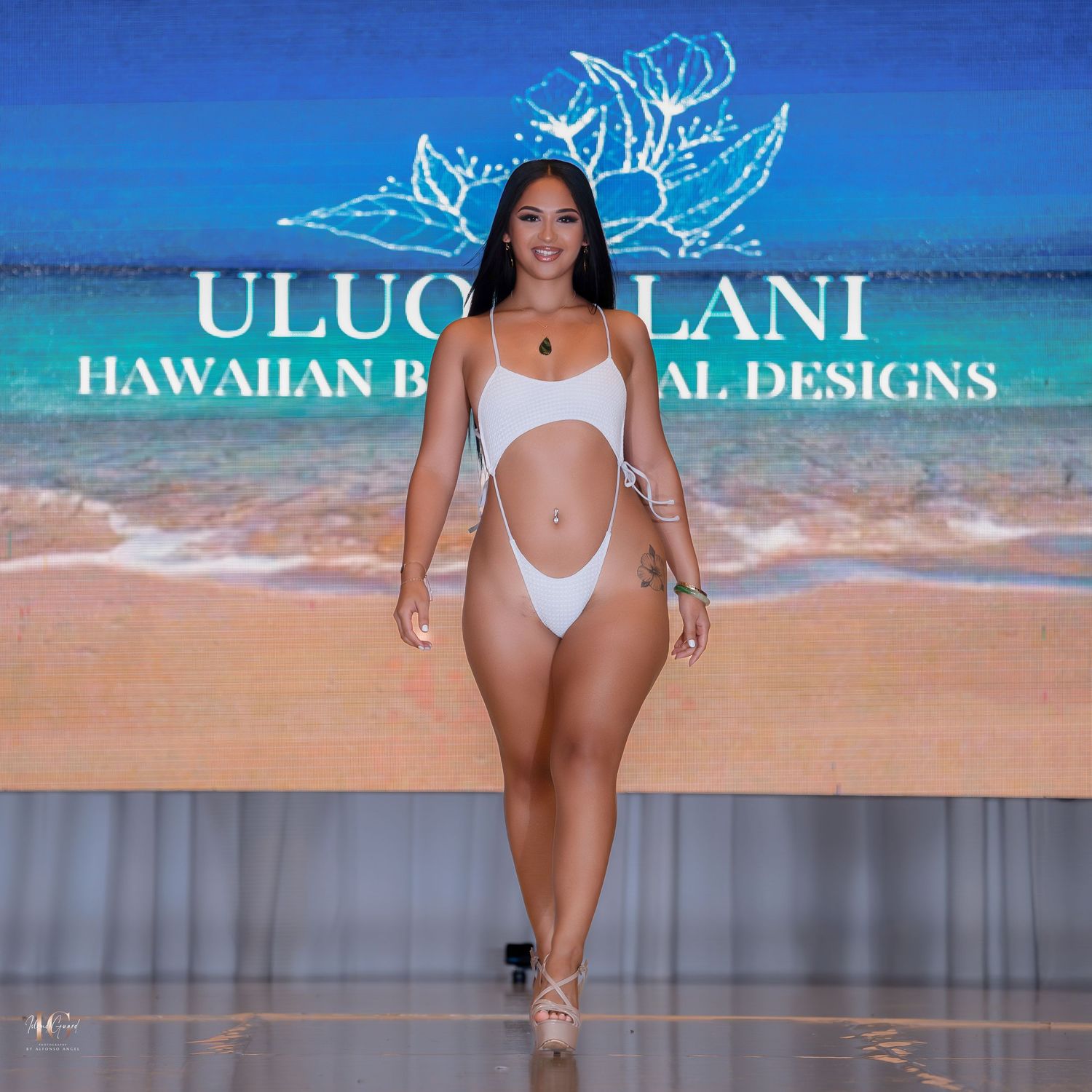 Swimwear fashion show on runway with beach-themed backdrop displaying Hawaiian designs.