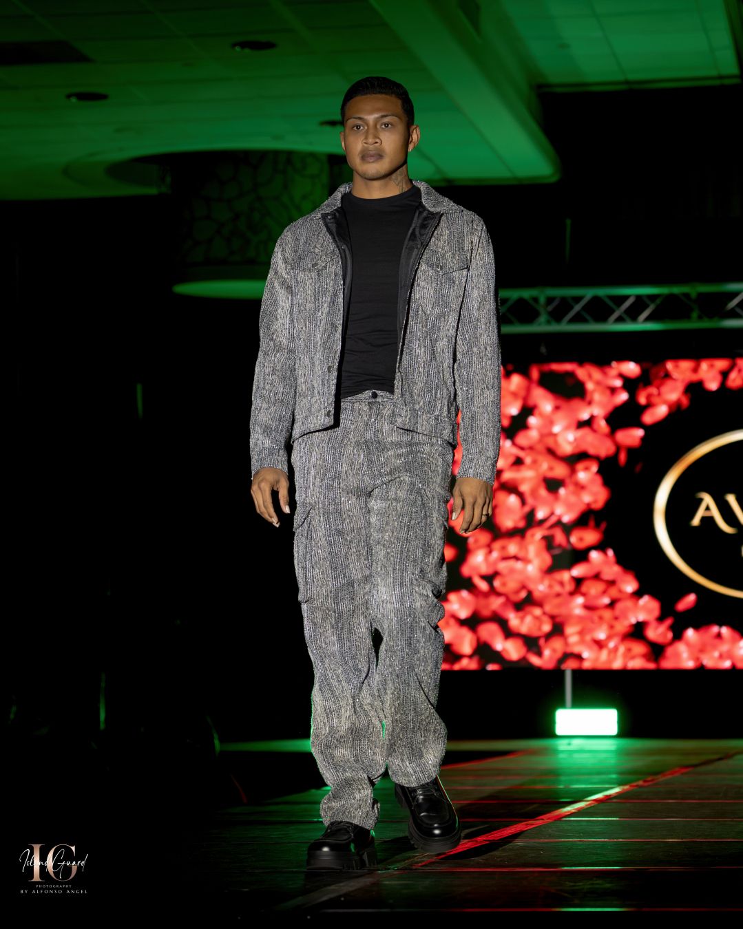 Grey textured tracksuit ensemble displayed on fashion runway with dramatic lighting and red backdrop.