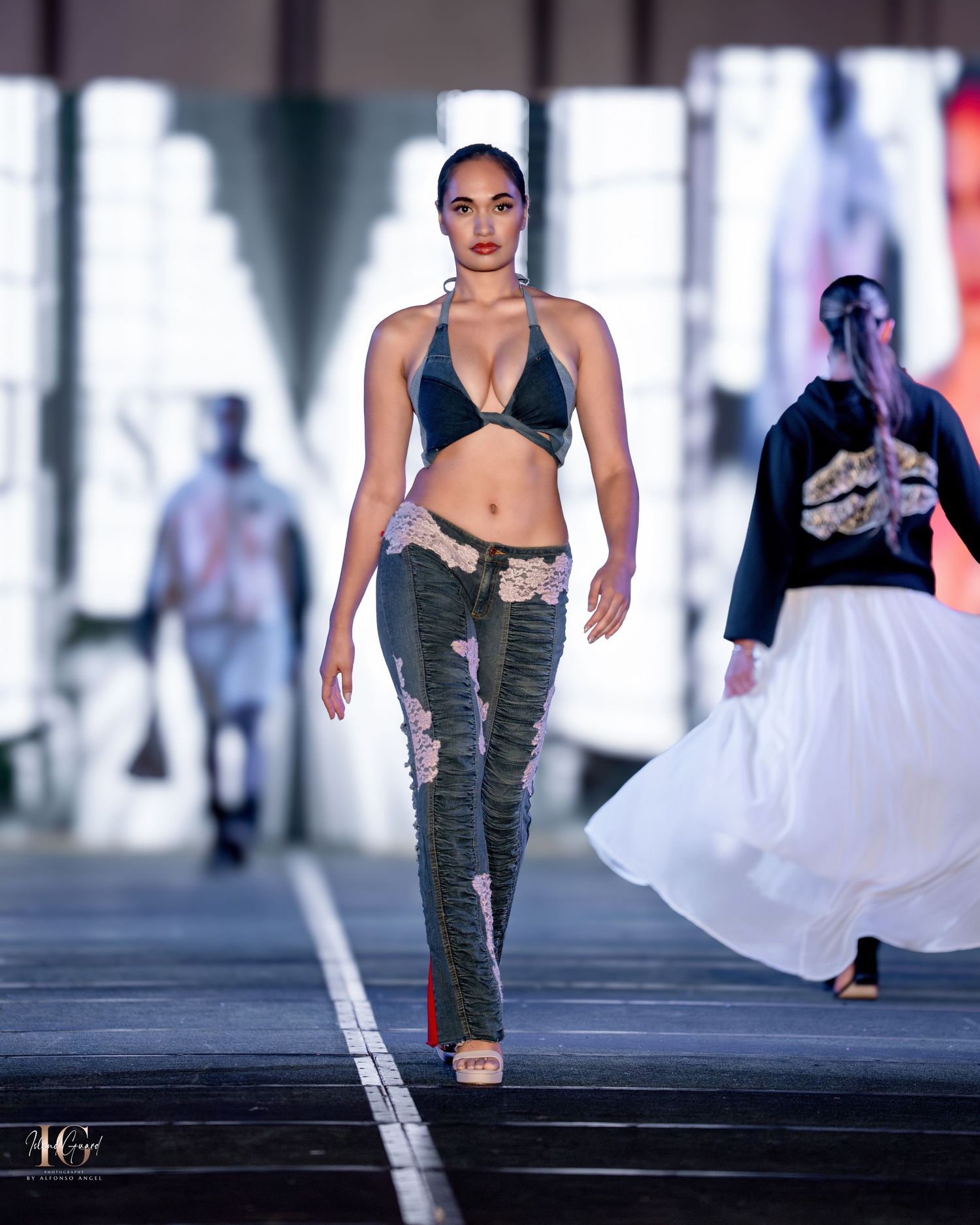 Model walks runway in black bikini top and camouflage pants with distressed details.