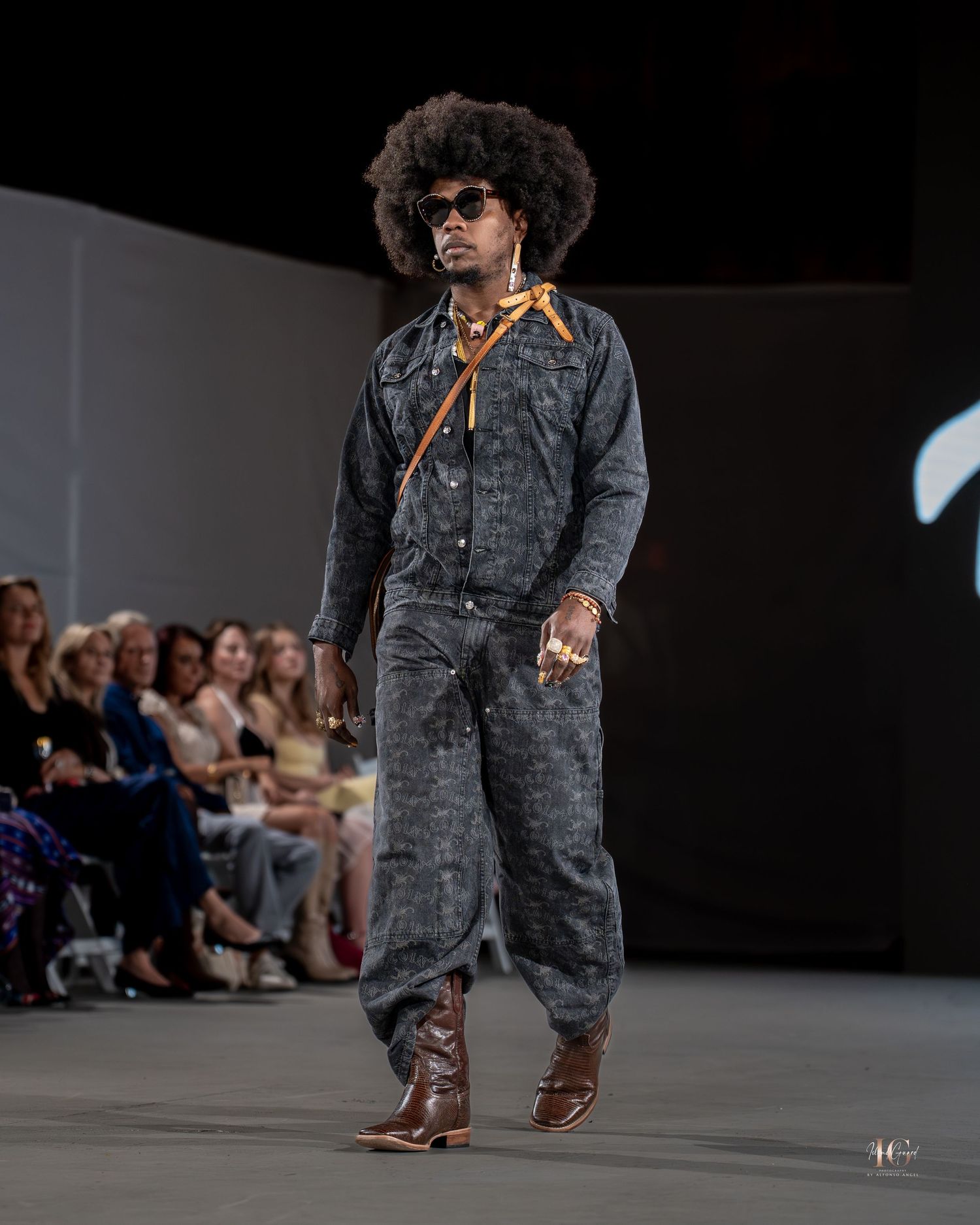 Model walks runway wearing gray textured suit and brown leather shoes during fashion show presentation.