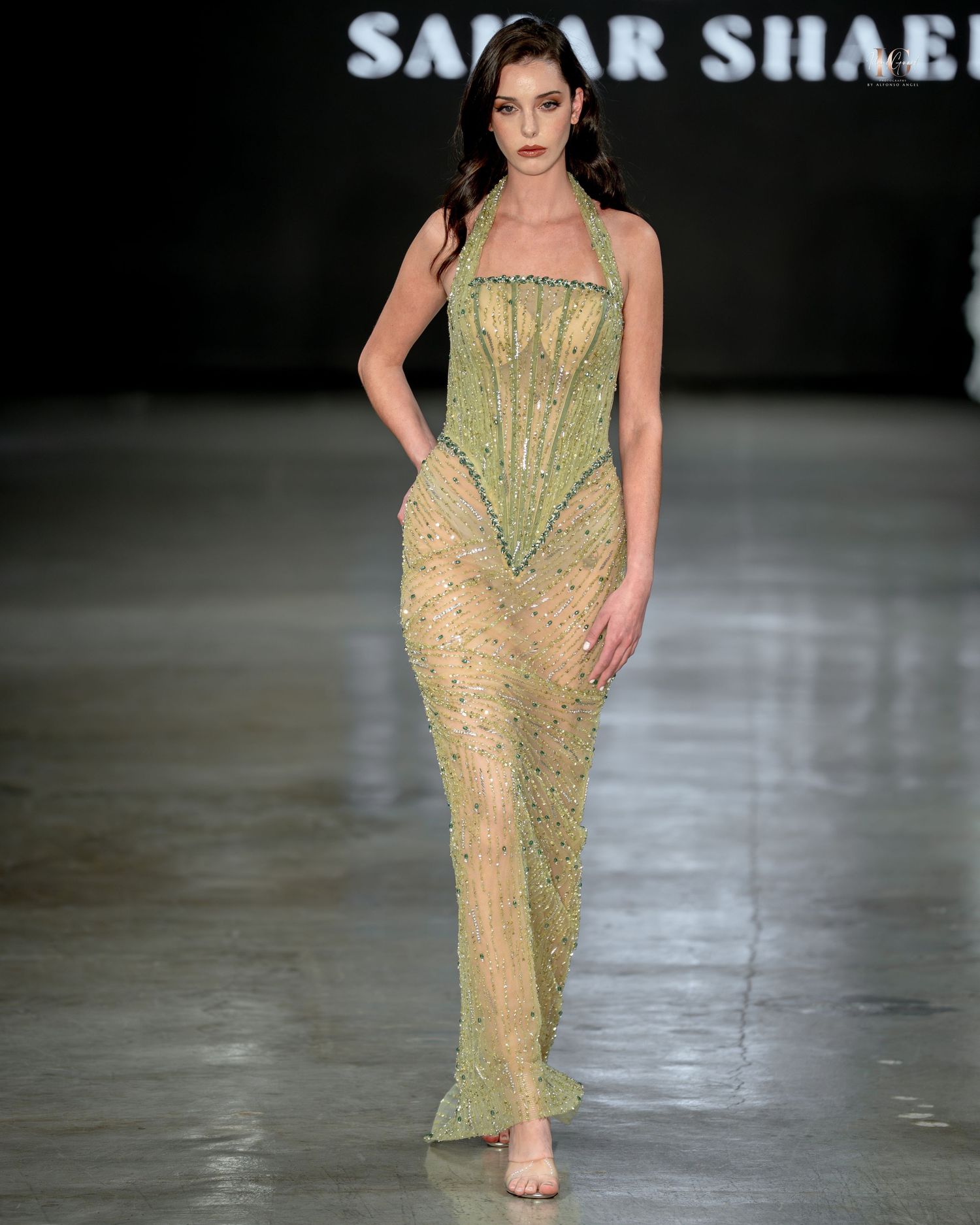A model walks the runway in a sheer beige and green embellished evening gown during the Samer Shaban fashion show.