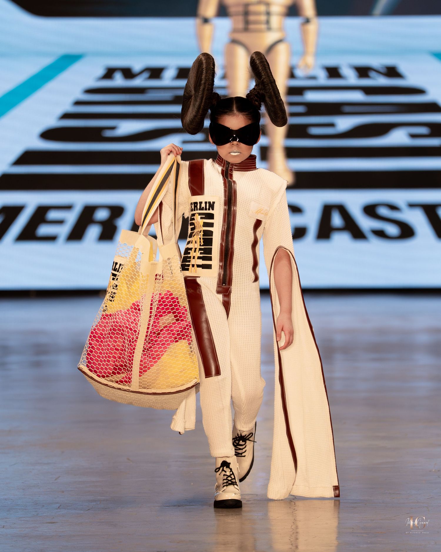 Models walk the runway wearing cream-colored outfits and accessories during a fashion show presentation.