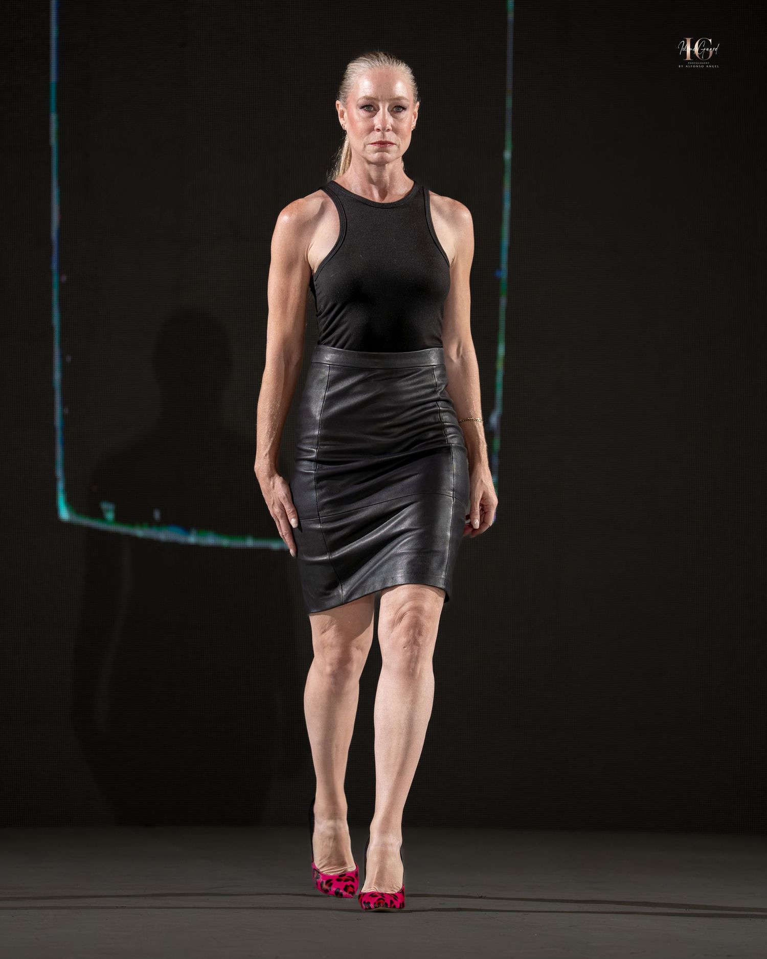 A dancer in a black dress and pink shoes performs a dramatic pose on a dark stage.