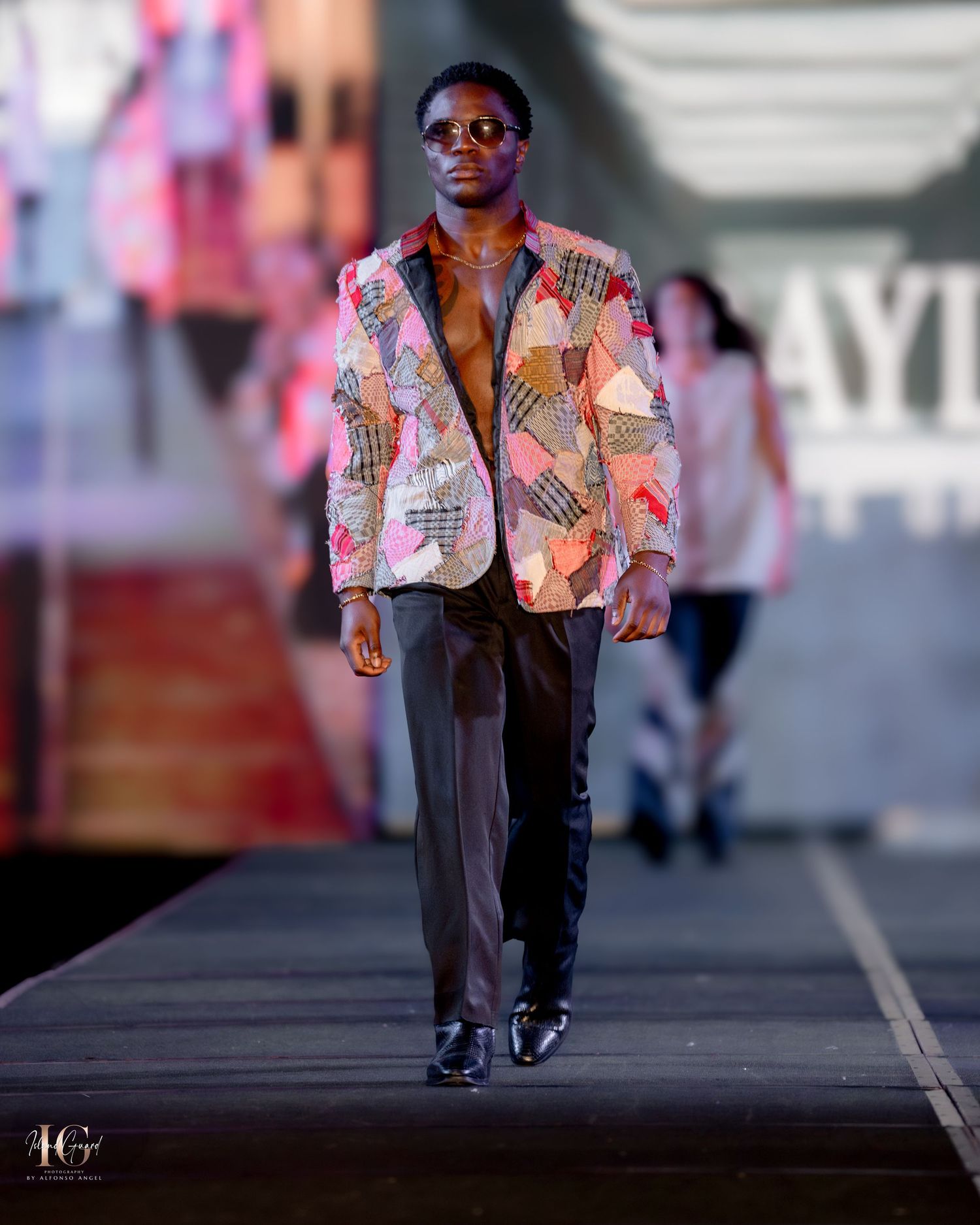 Colorful patchwork blazer styled with dark trousers and sunglasses on fashion runway.