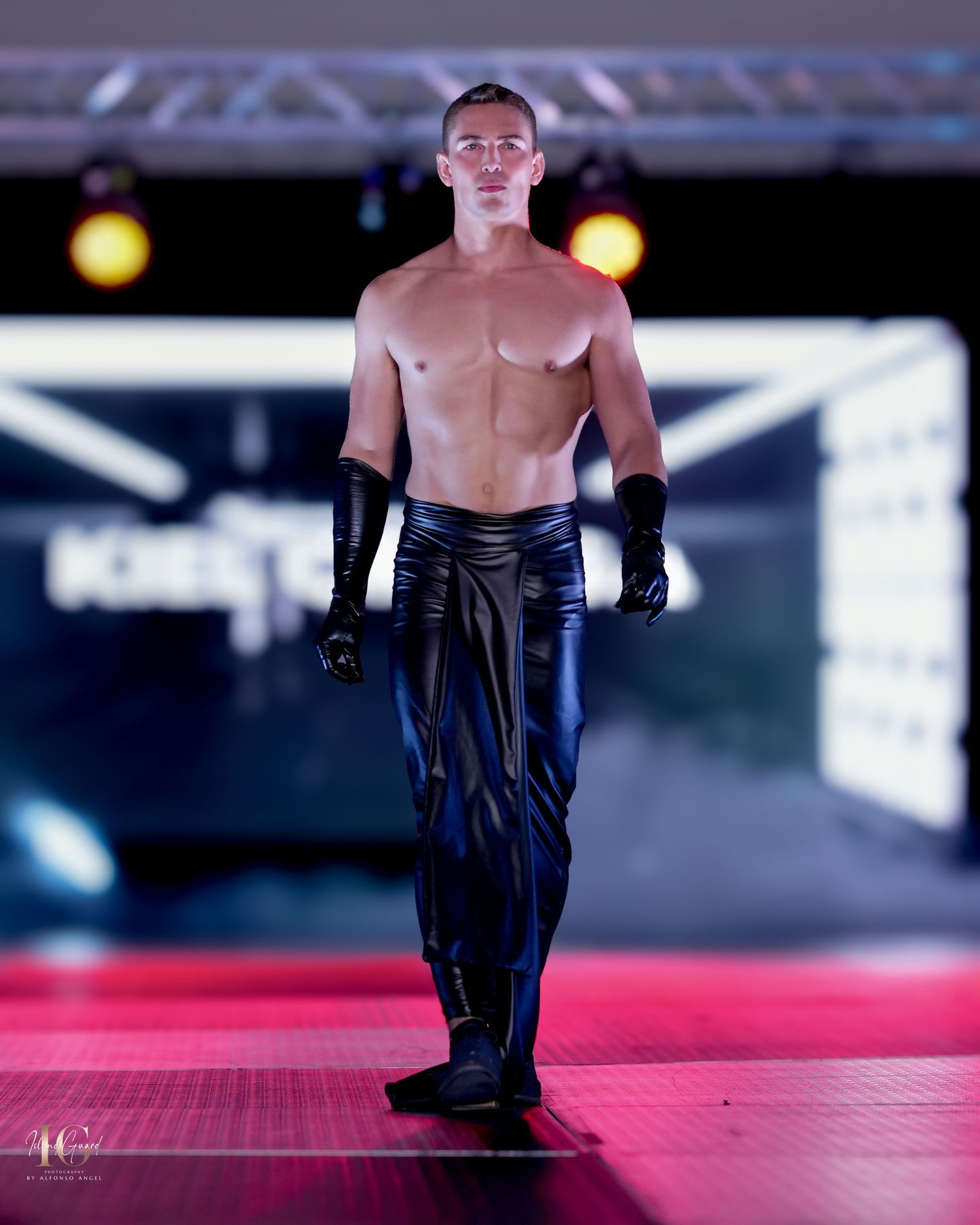 Bold black leather gloves and pants combination demonstrated on red-lit catwalk.