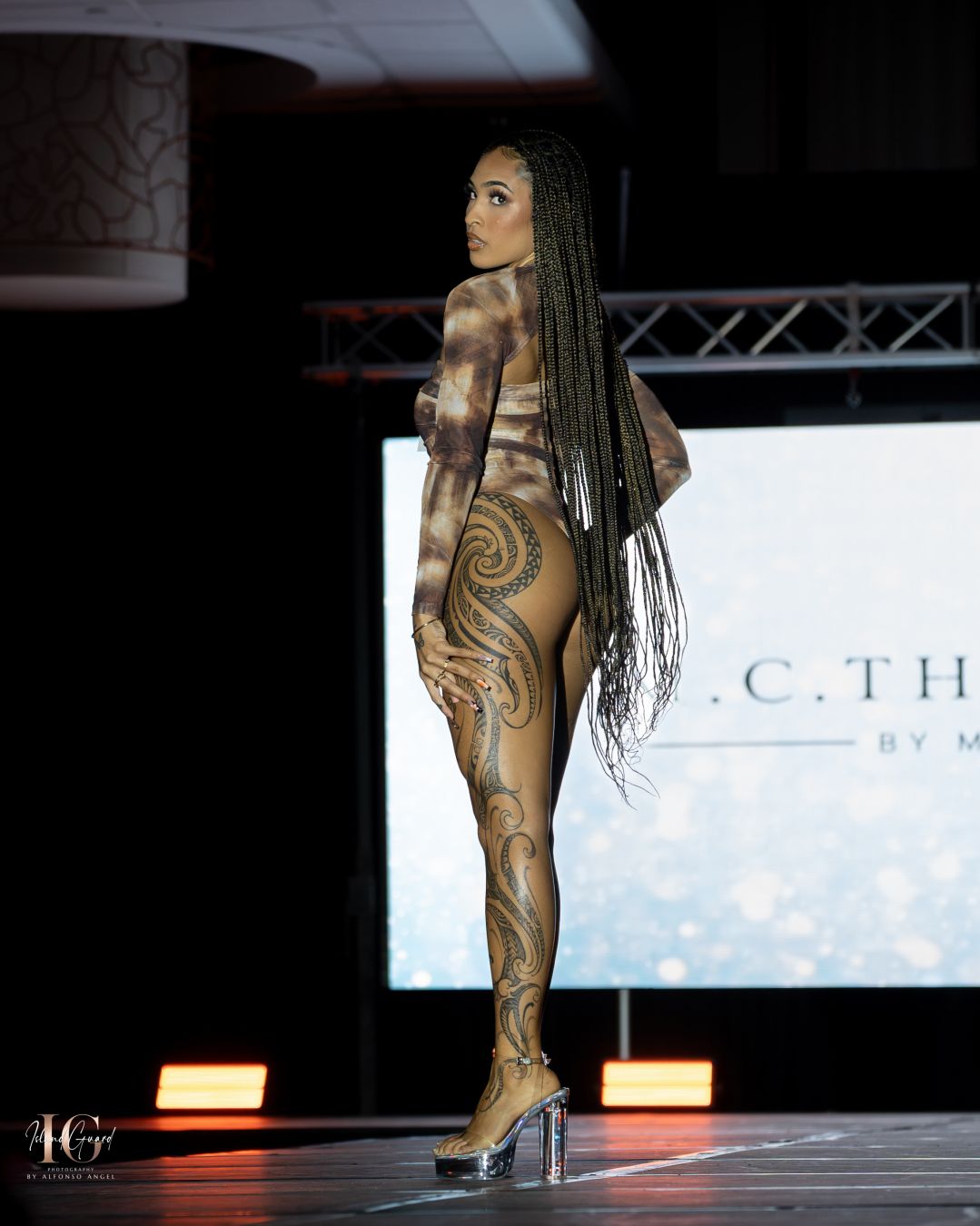 Model displays intricate body art with flowing braids at fashion show event.