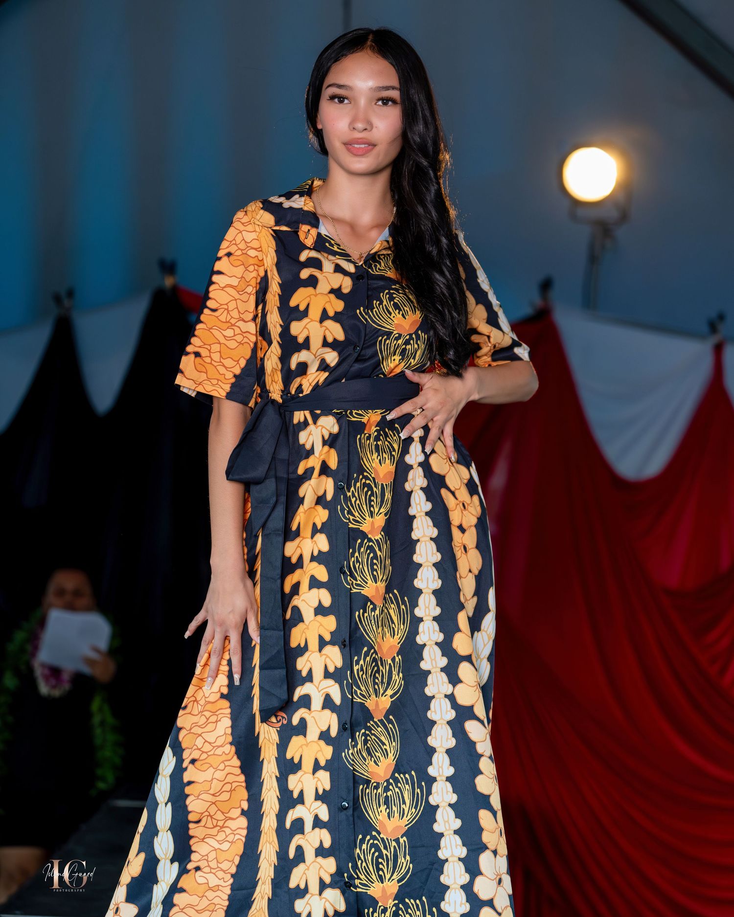Model displays traditional Pacific island inspired dress with yellow and white patterns on dark runway.