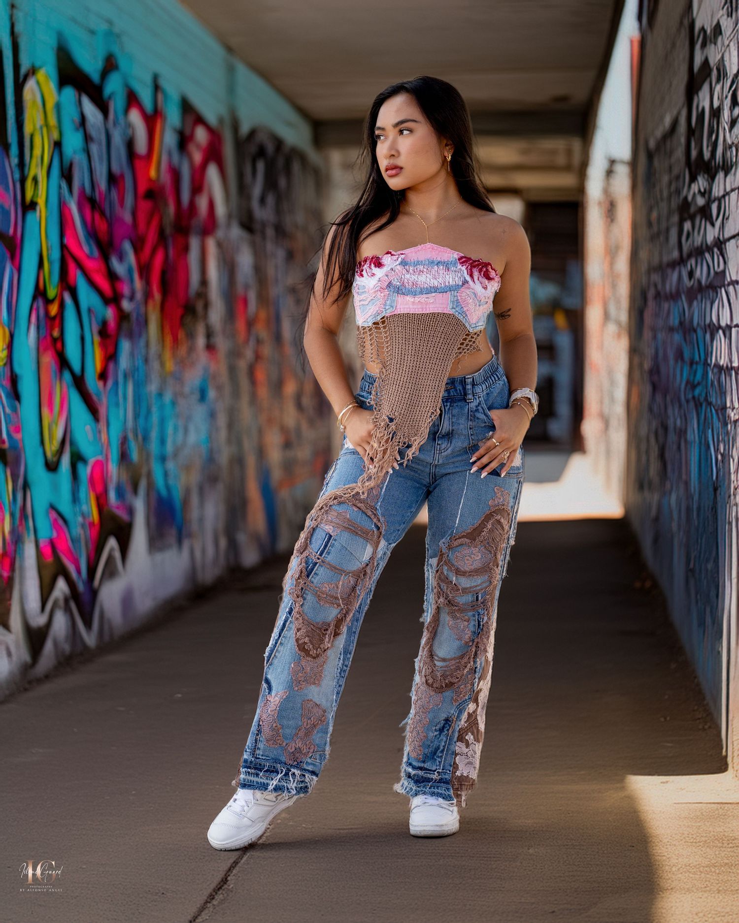 Urban fashion shoot in graffiti tunnel featuring distressed jeans and sneakers against colorful street art background.