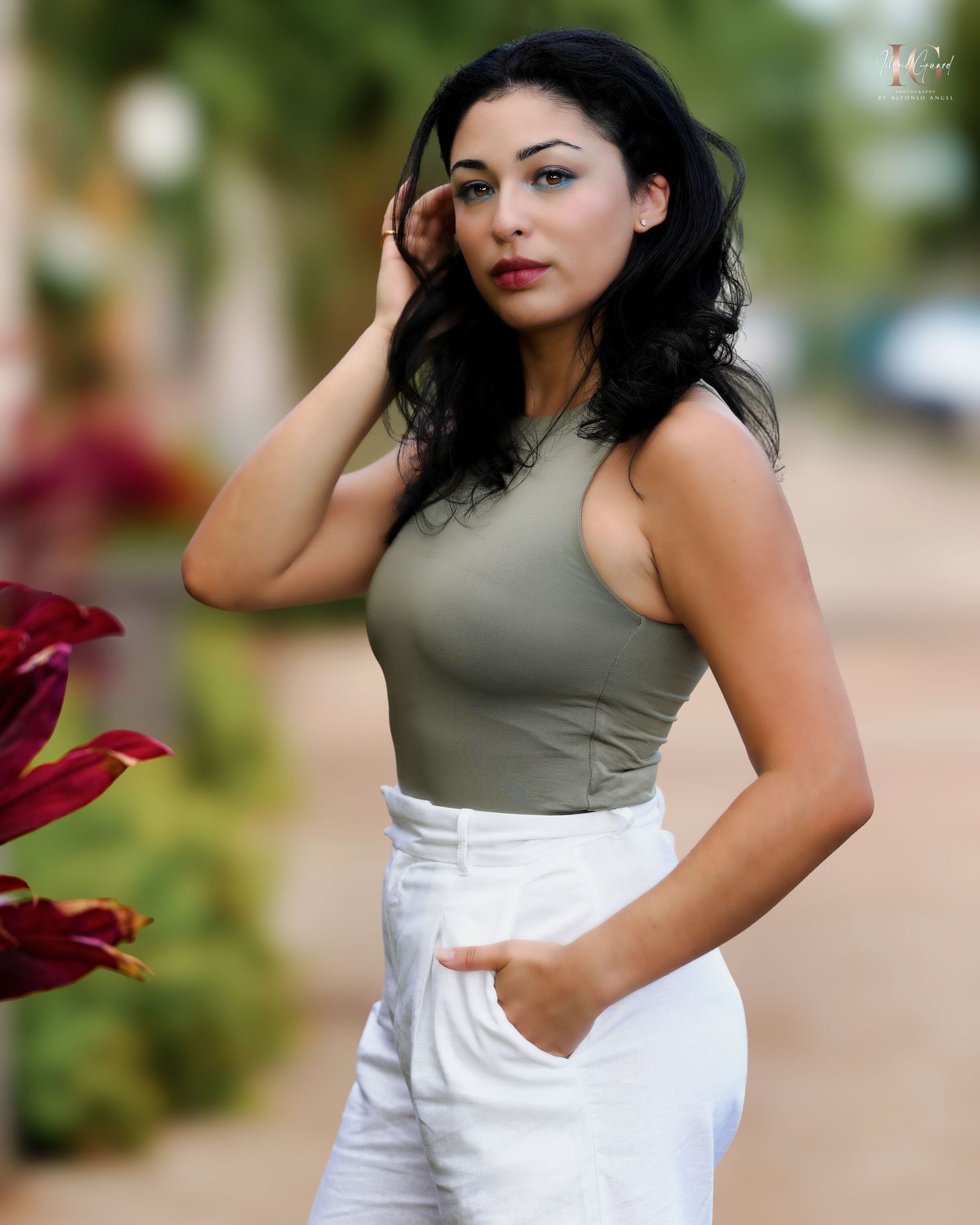 A fashionable outfit with a sleeveless olive green top paired with crisp white pants, photographed outdoors near red flowers.
