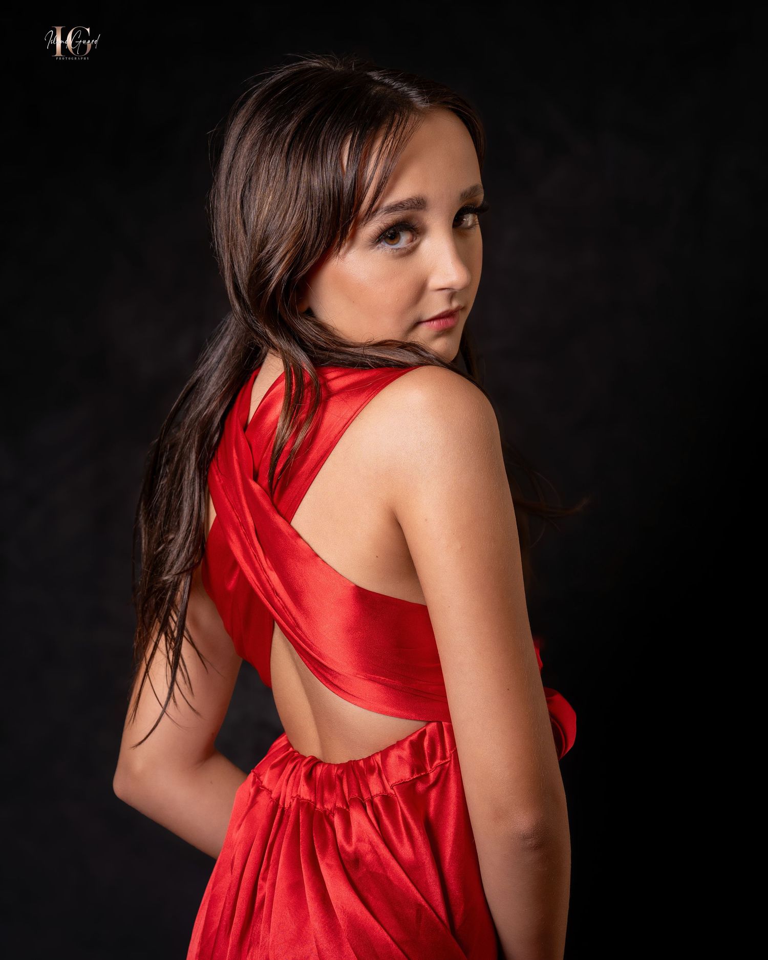 Woman in vibrant red dress poses gracefully against dark background creating dramatic contrast in studio photoshoot.