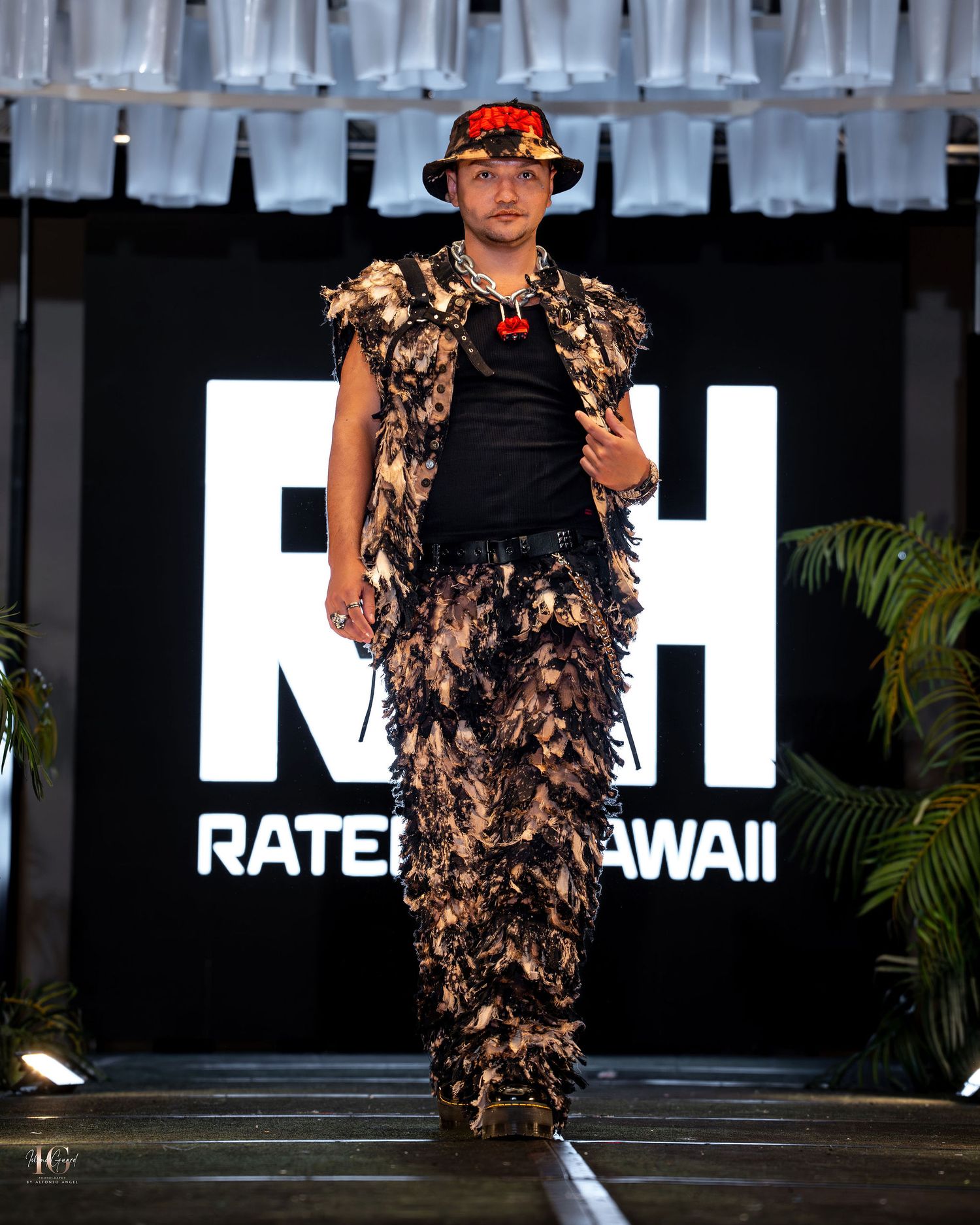 Model walks the runway in a dramatic black and brown feathered dress at a fashion show in Hawaii.