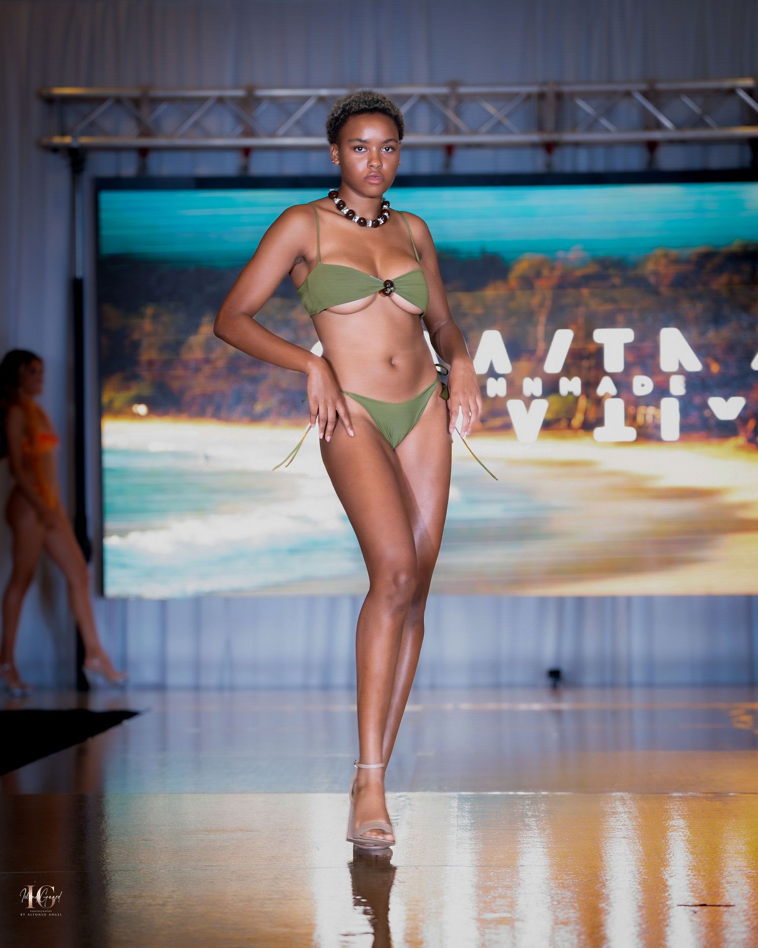 Models present beachwear collection on illuminated runway with tropical scenery.