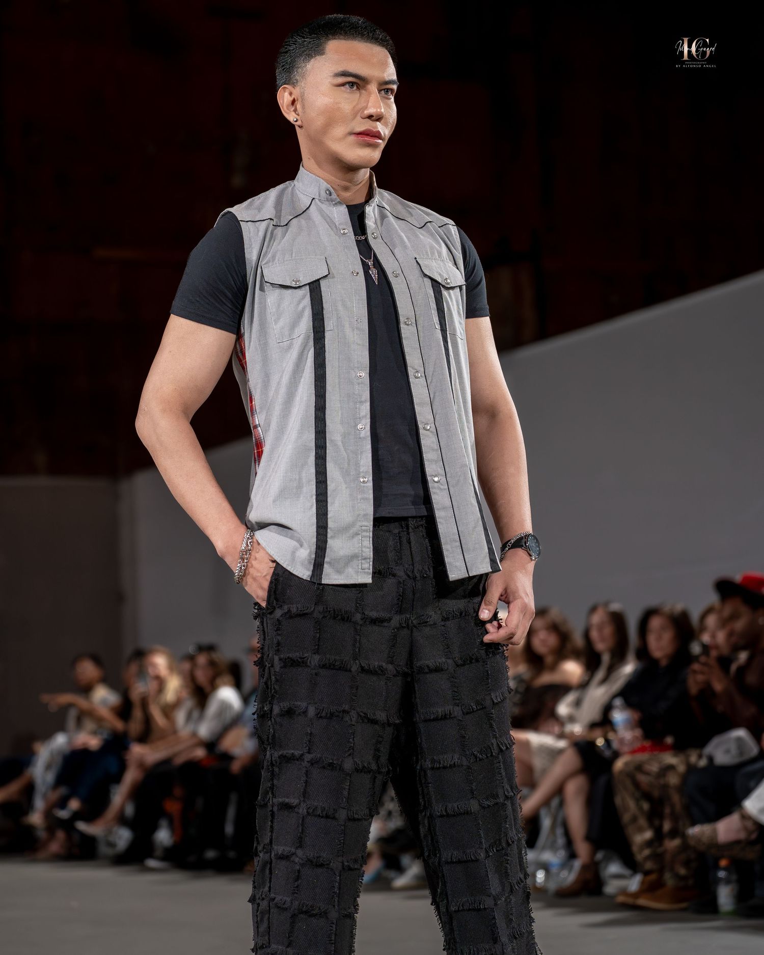 Fashion model on runway wearing black pants with cargo pockets and sleeveless grey vest during fashion show.