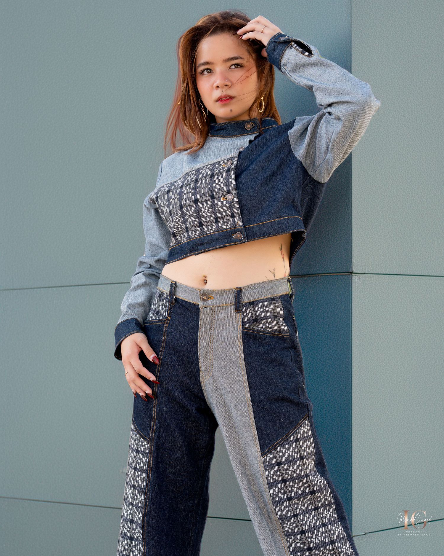 Model showcases patchwork denim and gray sweater combination in styled fashion photo series against blue wall.